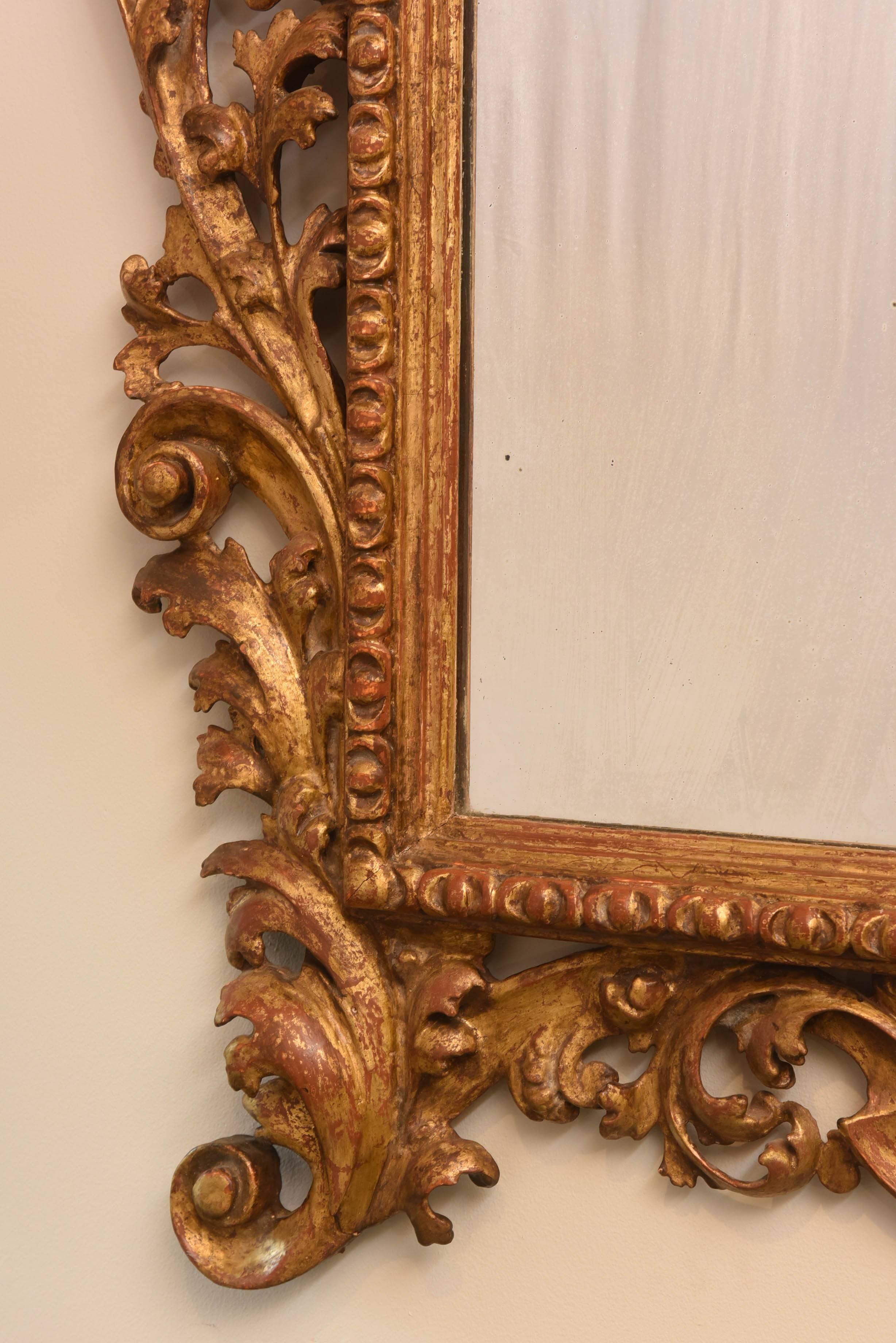 Mirror, having a rectangular, giltwood, molded border, with gadrooned edge, inside an elaborately carved, pierced frame of scrolling acanthus, surmounted by large palmette, with fold-over crown, flanked by curls and foliate decoration.