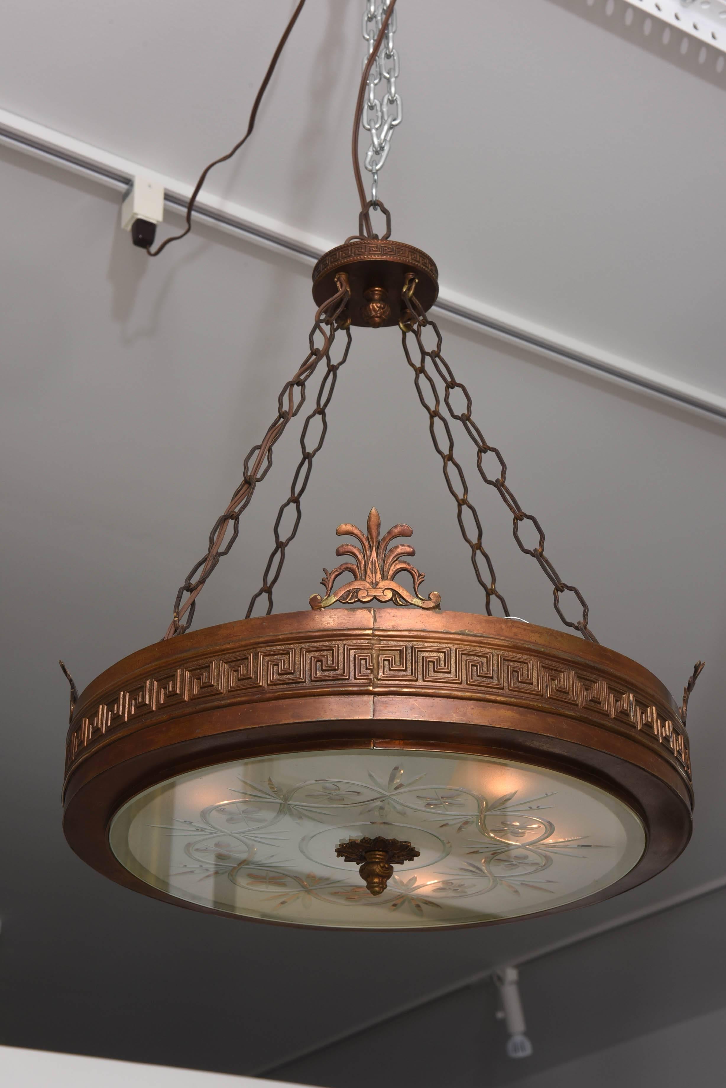 This handsome chandelier dates from the 1920s and is fabricated of cast bronze and a central glass-diffuser with cut and frosted details. The main frame is detailed with a Greek key border and four stylized palmettos. 

Note: This chandelier could