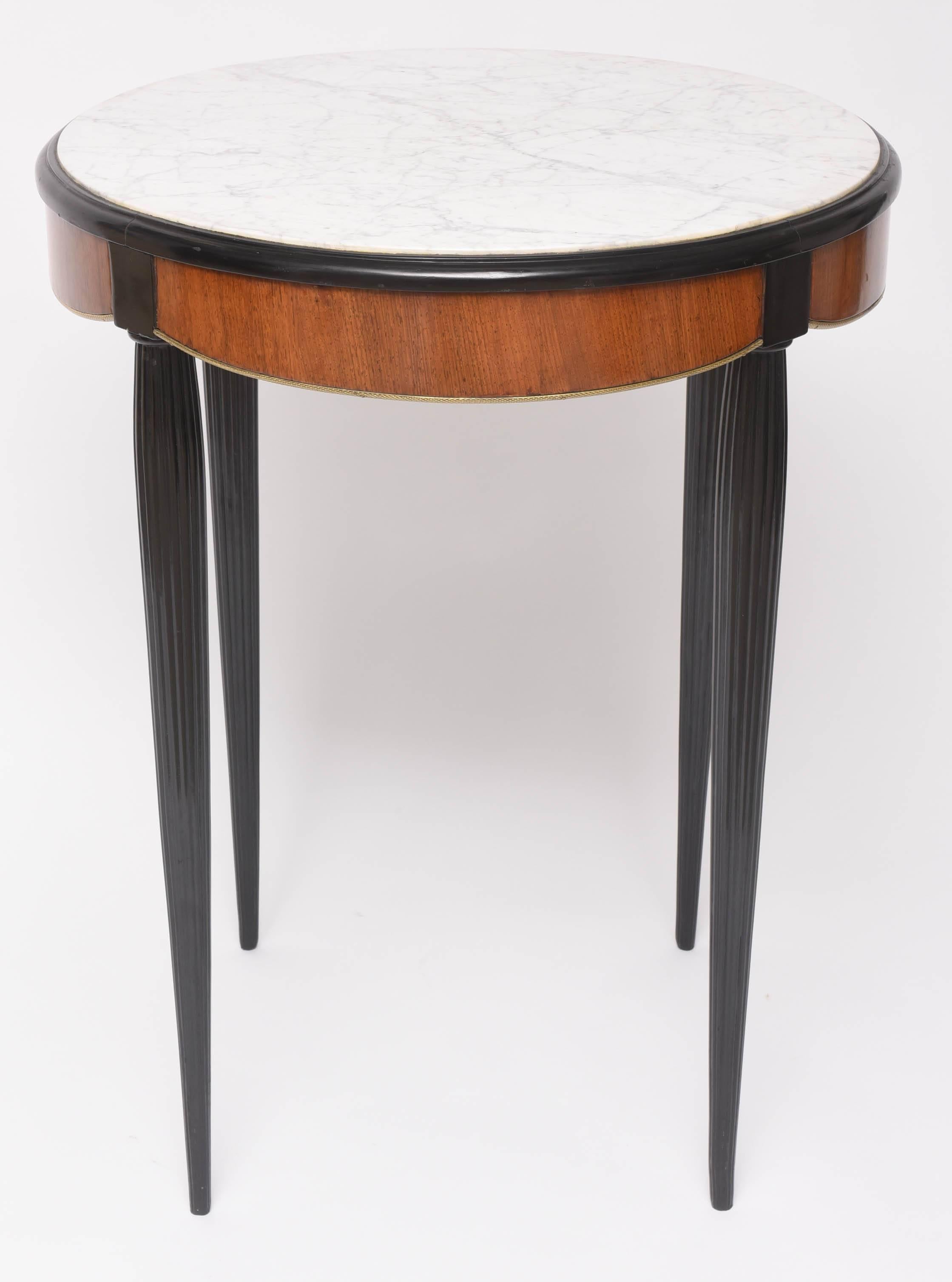This beautiful and stylish Art Deco style table could be used as a side or center table. With its delicate features of soft-colored Carrara marble inset top, fluted legs and scalloped, mahogany wood apron edged in bronze-doré trim it epitomizes the