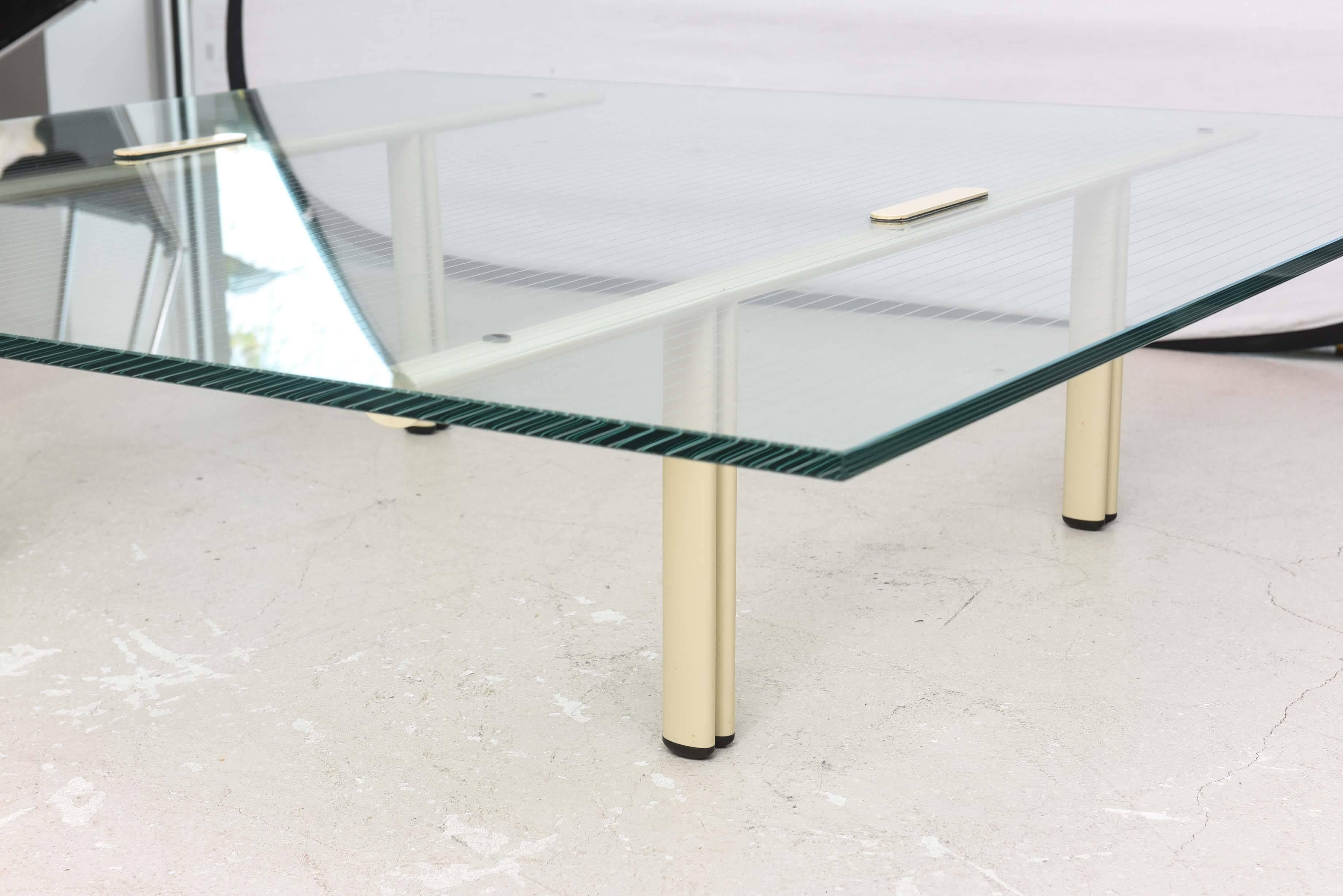 Large coffee table with light cream color enameled metal legs and lightly etched grid pattern on the square glass top.