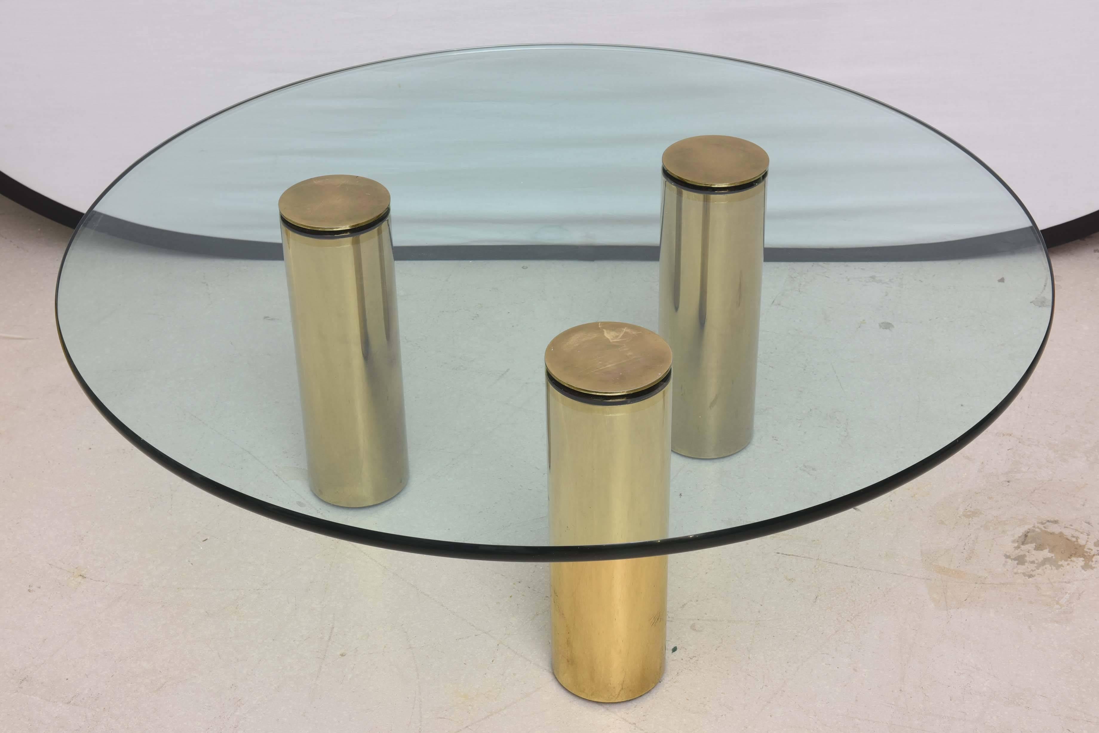 Geometric cocktail table with three tubular brass legs and circular glass top.