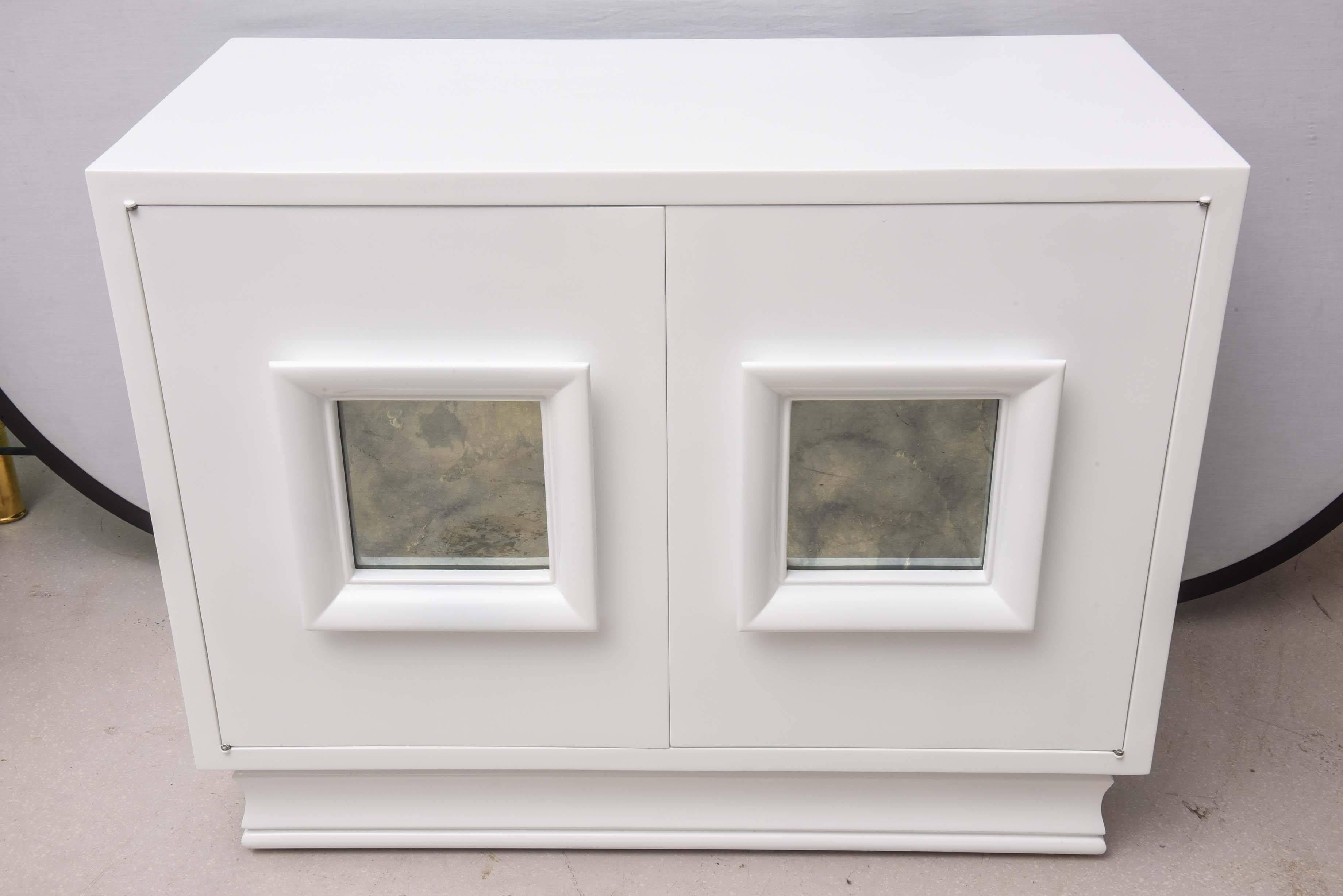 Pair of white lacquered Hollywood Regency chests with smokey mirrored panels accenting the front doors.