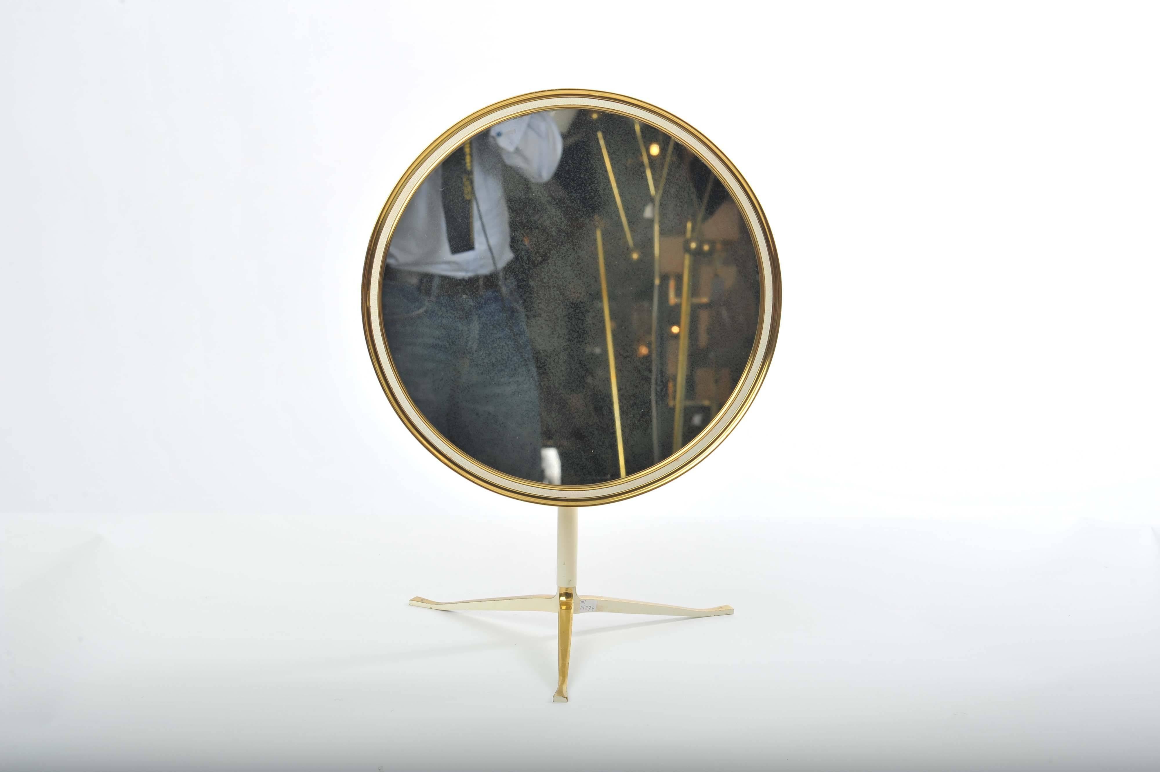 Elegant adjustable table mirror in brass with creme edging sits on tripod legs.