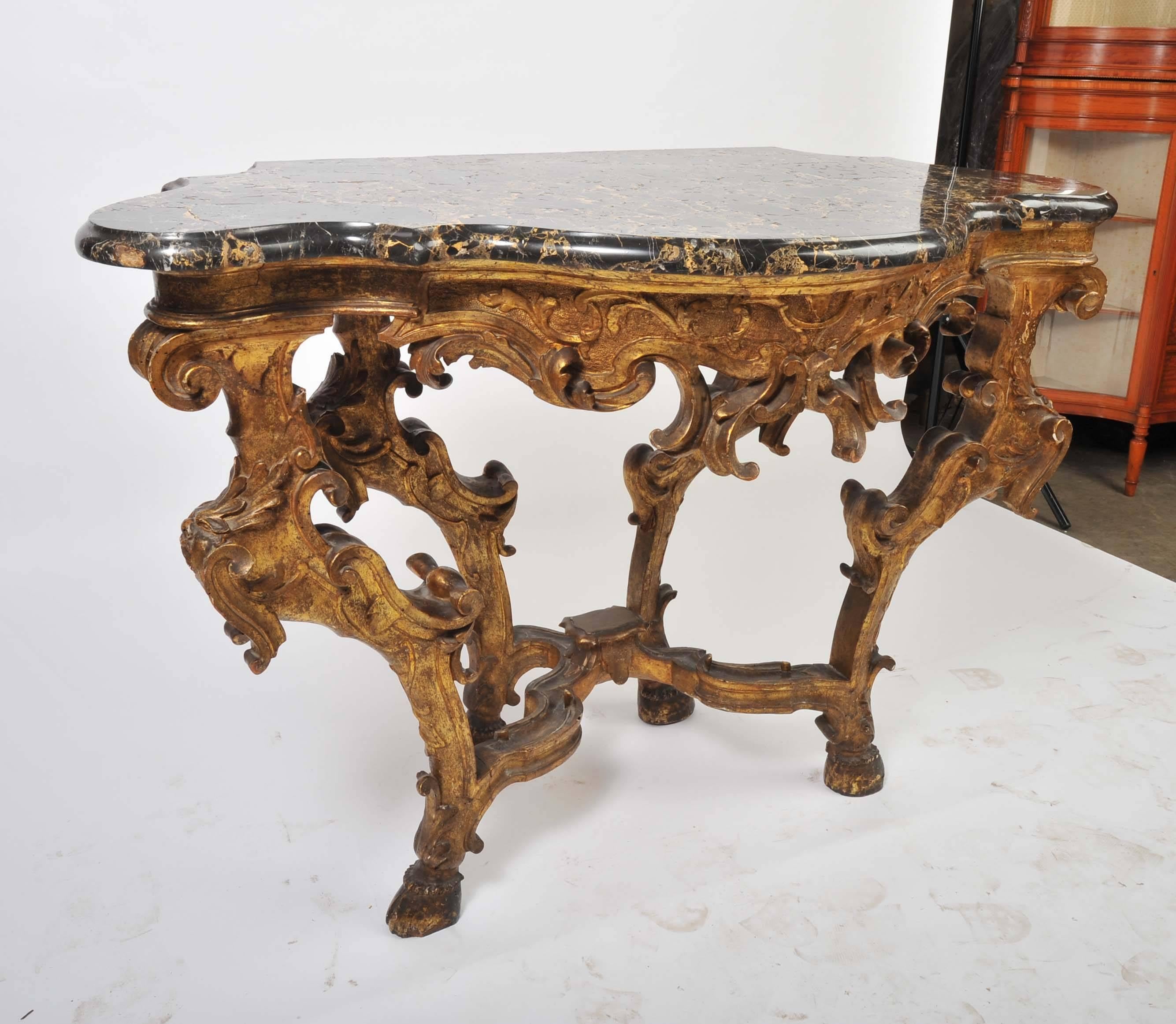 A wonderful pair of carved giltwood 18th century Venetian, marble-topped console tables. Having classical scrolling foliate decoration to the frieze and legs which is then united with a stretcher below. Having the original marble tops.