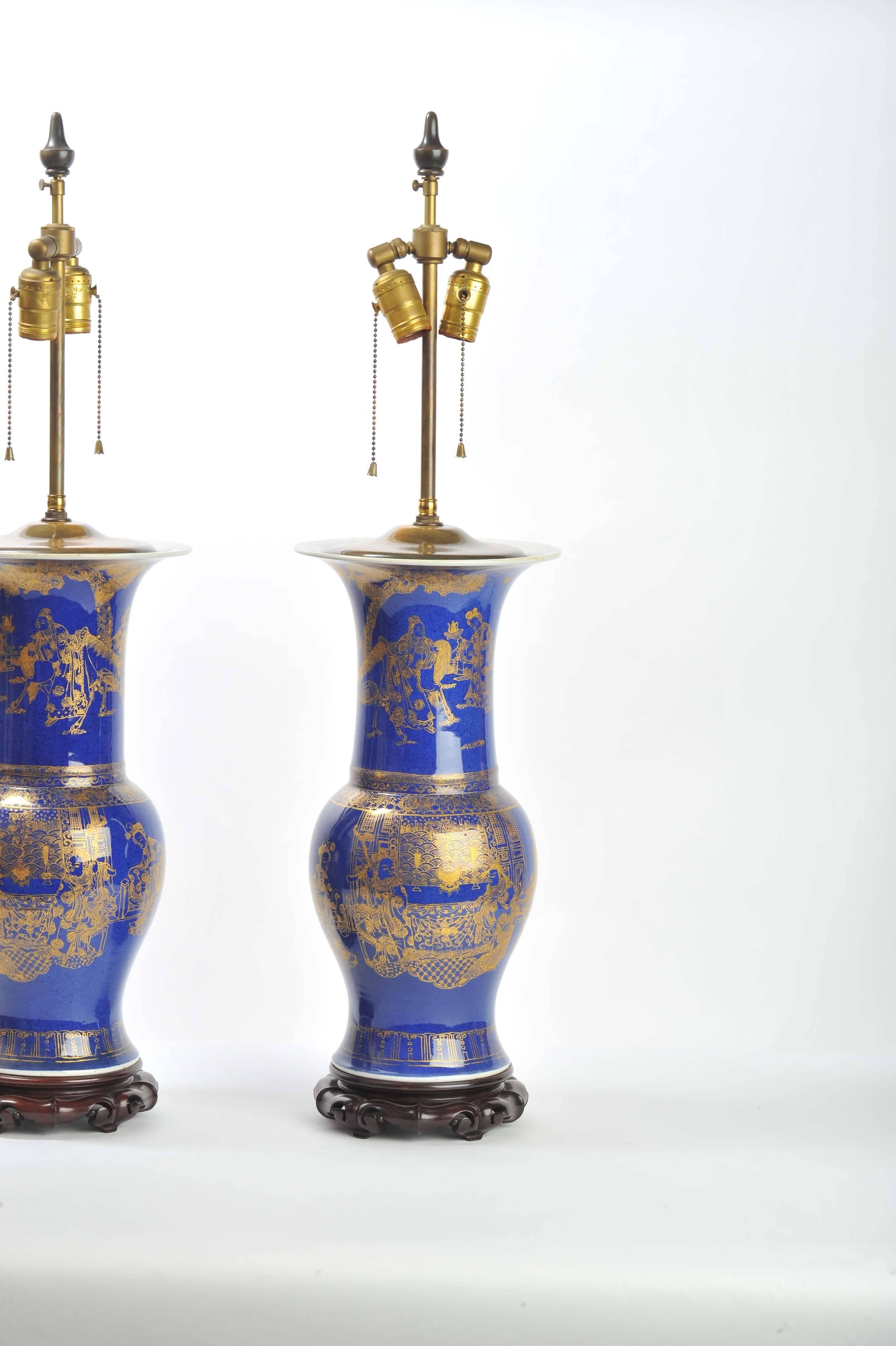 A good quality pair of Chinese 19th century powder blue vases, converted to lamps. Having gilded decoration, depicting classical Chinese scenes and raised on a hardwood carved base.