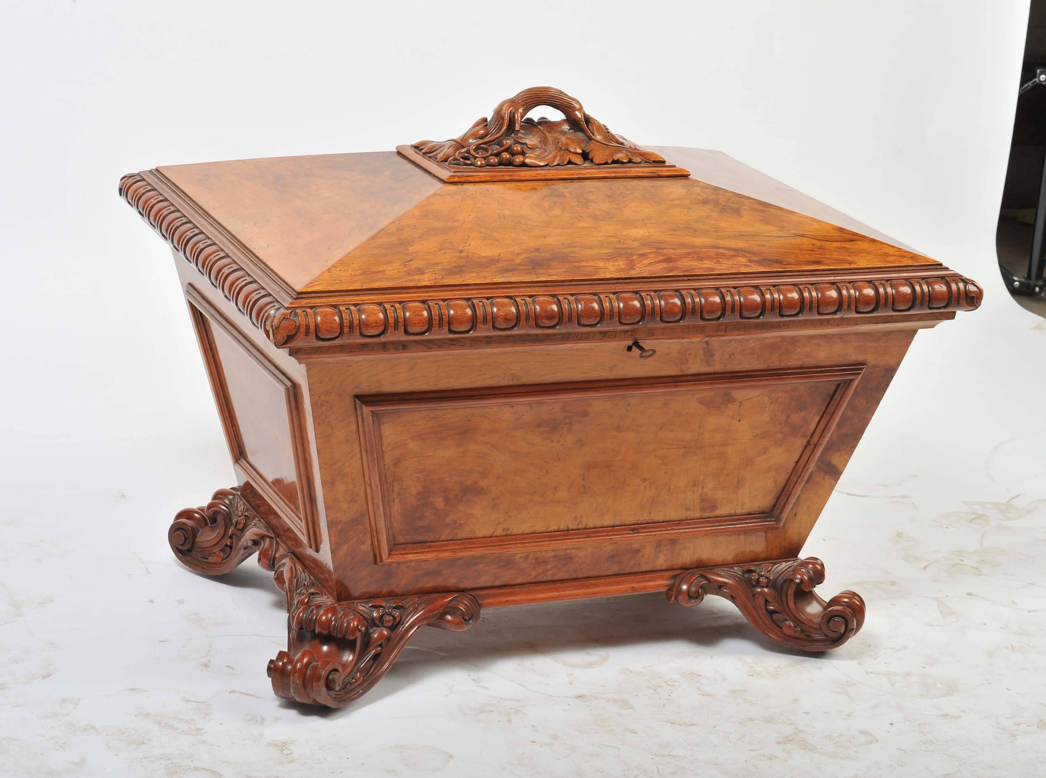 A very good quality late Regency period figured oak celleret, having a carved vine leaves and grapes to the handle, hinged top with lead liner. Carved gadrooned moulding, panels to the sides and raised on classical scrolling feet and brass castors.