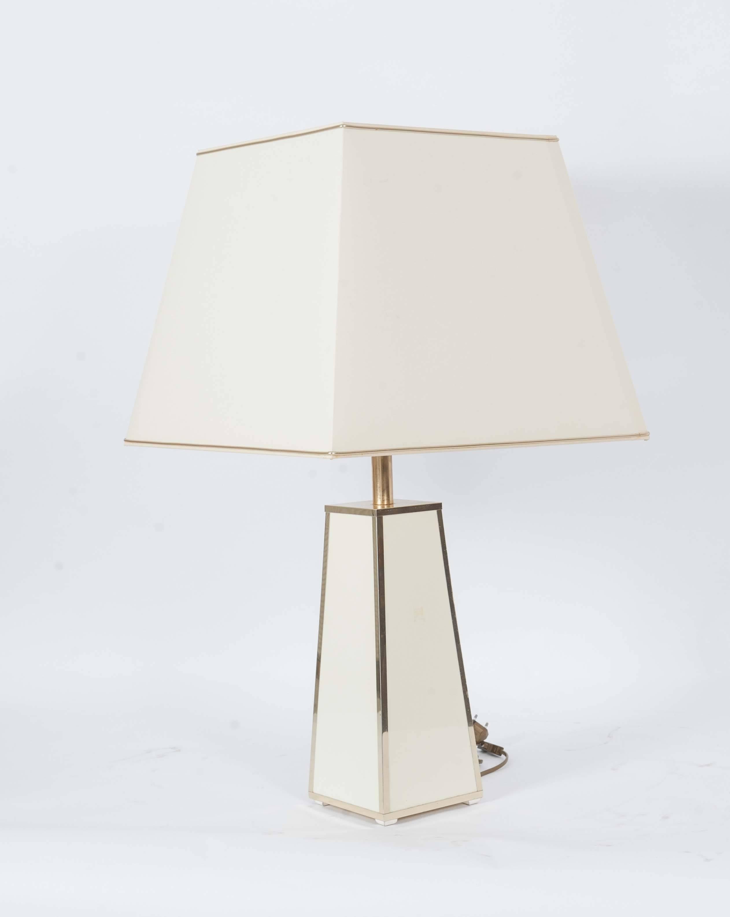 This rather large table lamp radiates a chic club atmosphere. Its square pillared foot has golden corners and creme colored planes. 
The shade is also square tapered which ensures the warm lighting. 

The measurements of the shade are:
Height 36