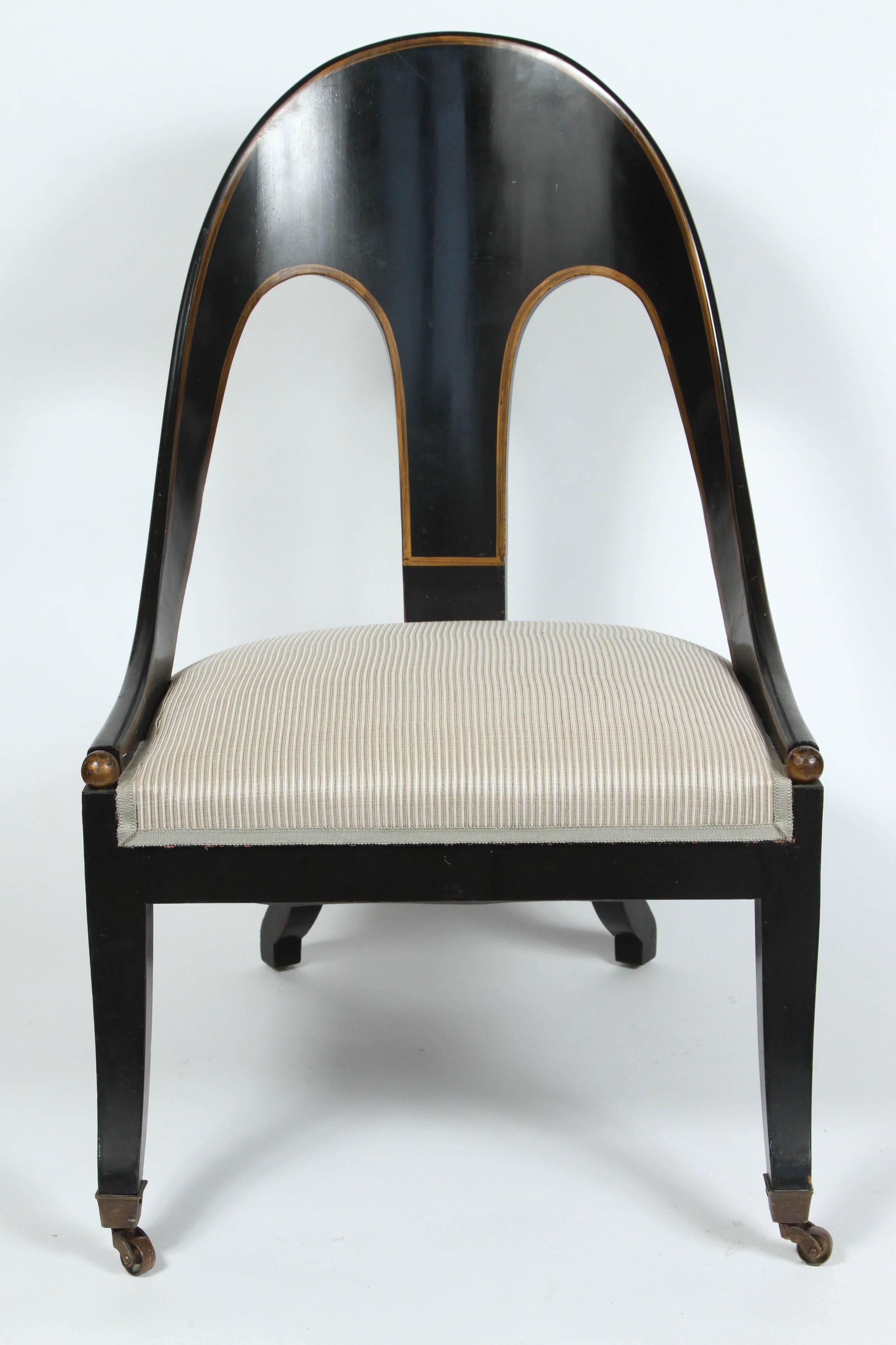 A pair of Regency-style spoon back lounge or slipper chairs, circa 1960. Chairs have a black lacquered finish with gold accents. To the front of the arms and feet, are gold ball finials. The seats are newly reupholstered.