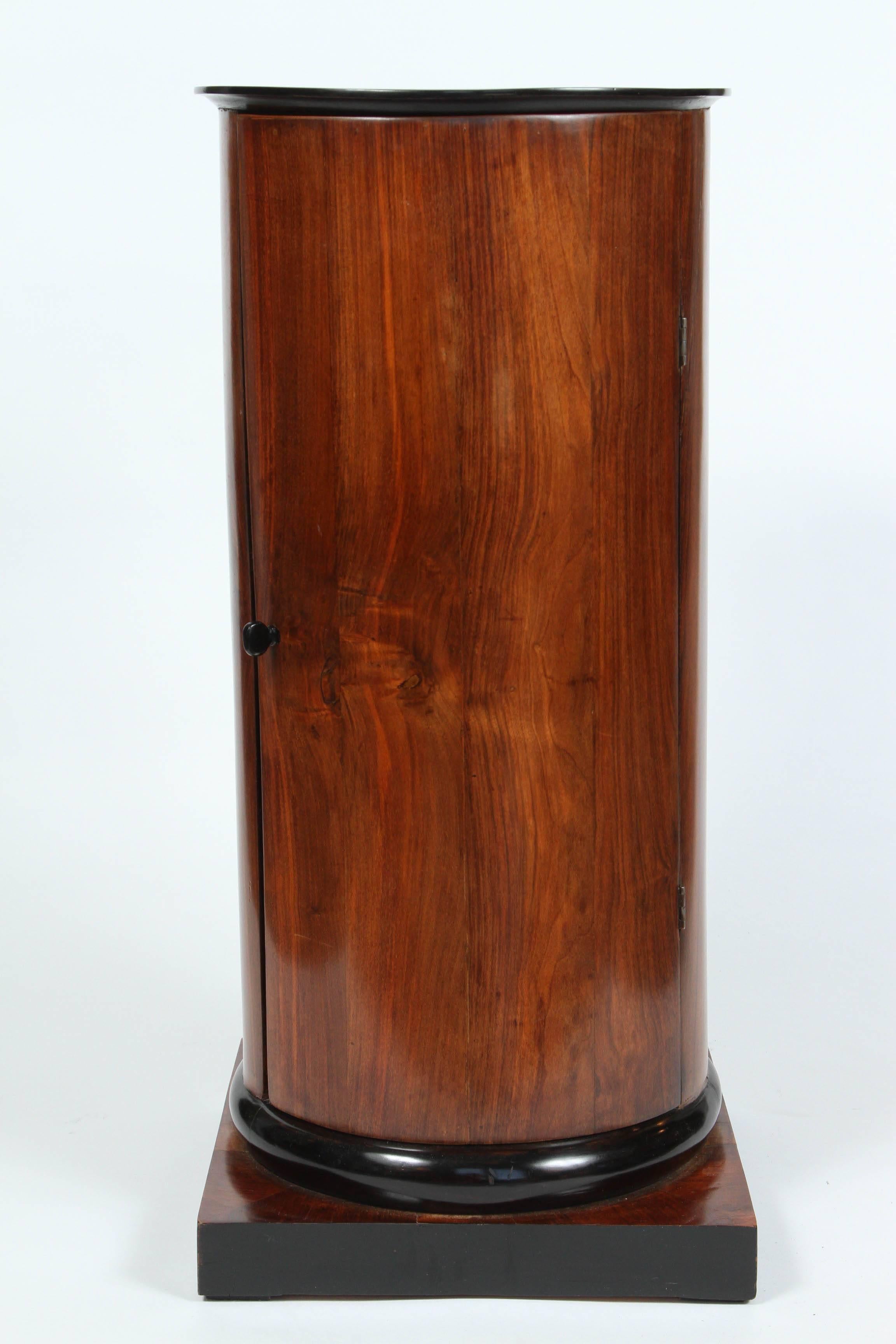 A walnut and ebonized wood biedermeier cylindrical pedestal cupboard, 19th century.