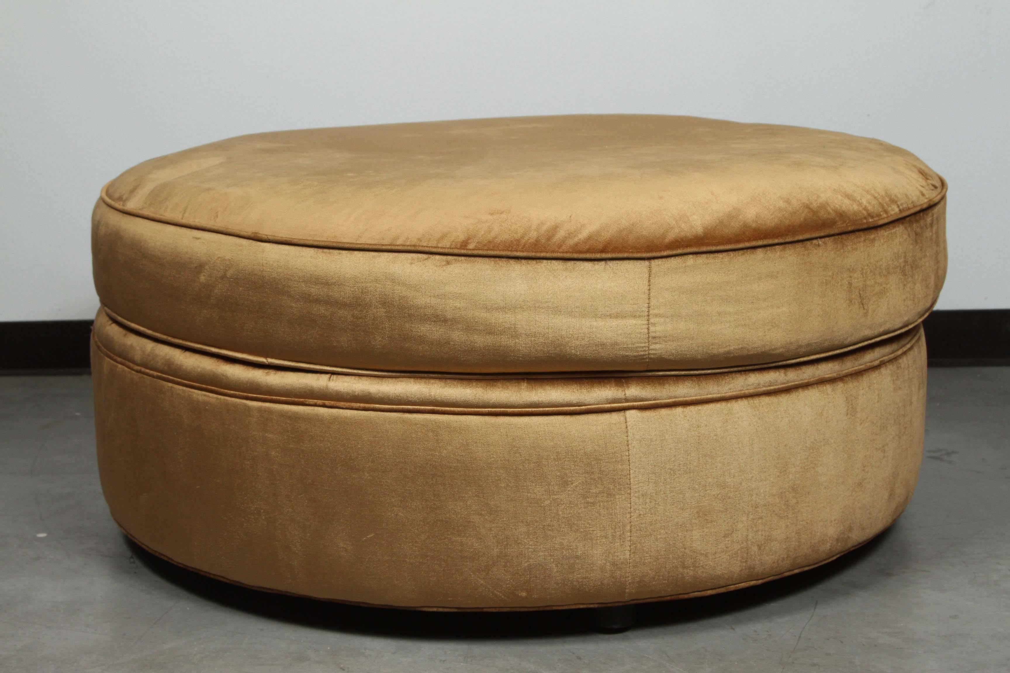 Large circular ottoman upholstered in a gold velvet with copper tones.