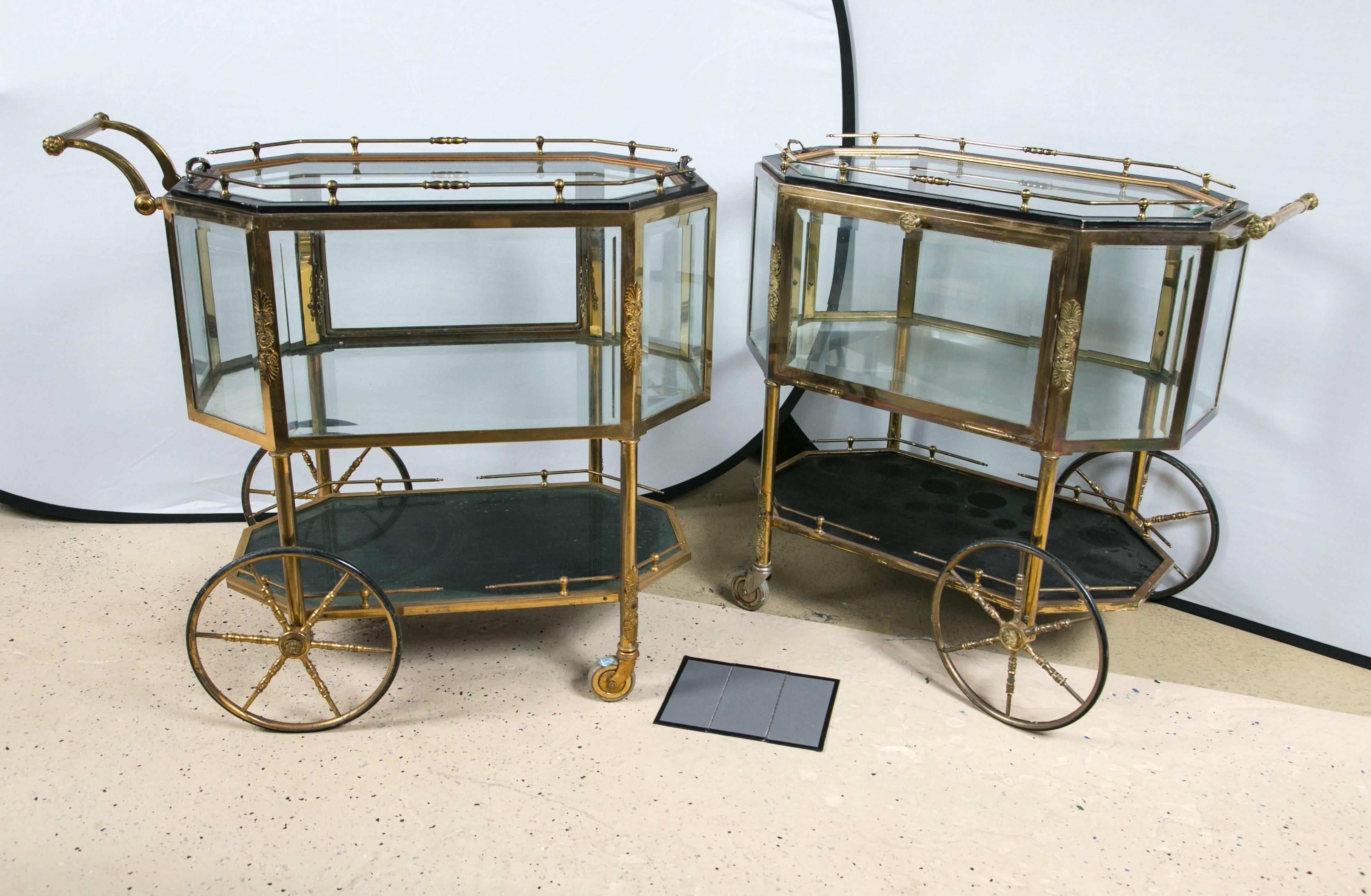 Pair of bronze and glass vitrine serving tea wagons. The large brass wheels make this rolling cart easy to maneuver and give the whole a palatial look. . The all beveled glass case having pull down sides to allow for easy access. The upper and lower