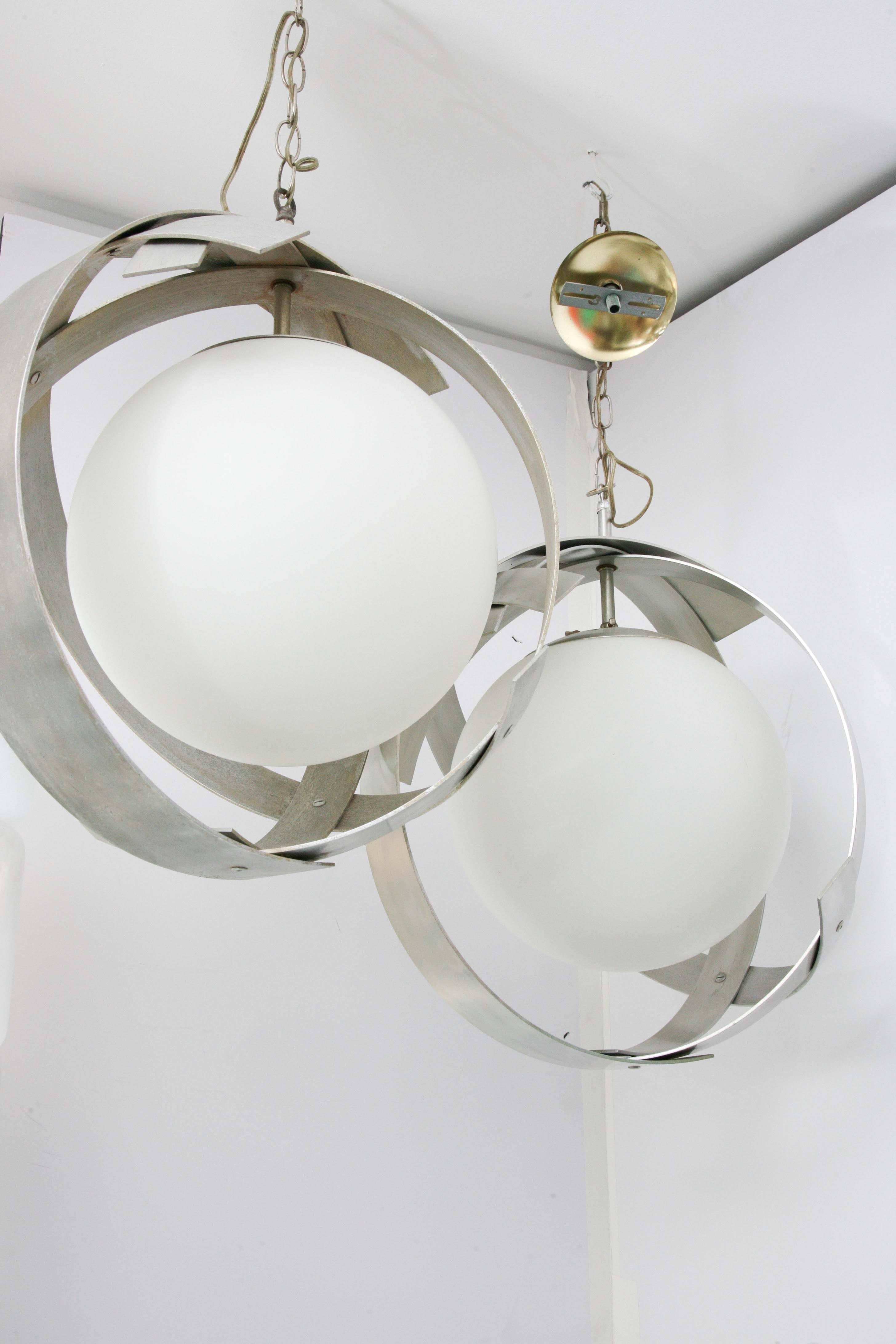 Solid alum. Rings with white satin glass globes. One lamp has Arredoluce label and the other has slightly wider bands. Both pendants hang from chrome chains and electrical is original and in working order. Priced individually. There is enough chord