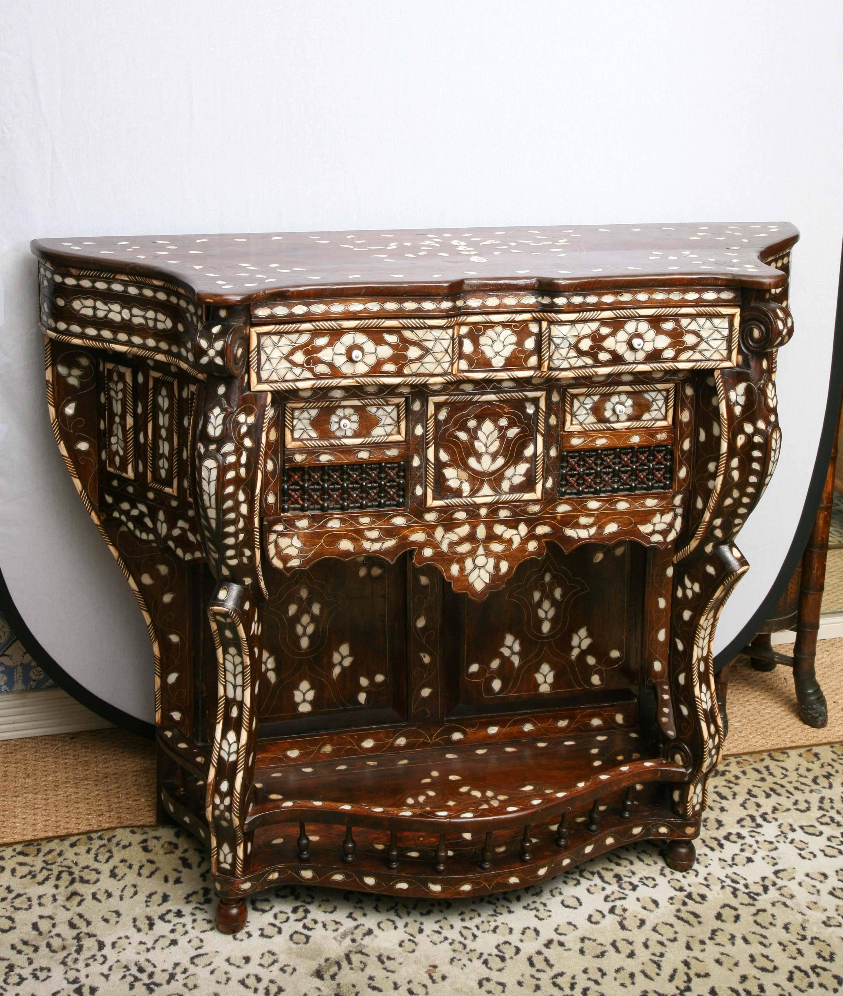 
Superb Syrian mother-of-pearl inlaid console, the shaped top inlaid with floral tendrils, surmounting the conforming case having one over two drawers with ball and spindle detailing and shaped pendant apron rising on C-scroll legs conjoined by a