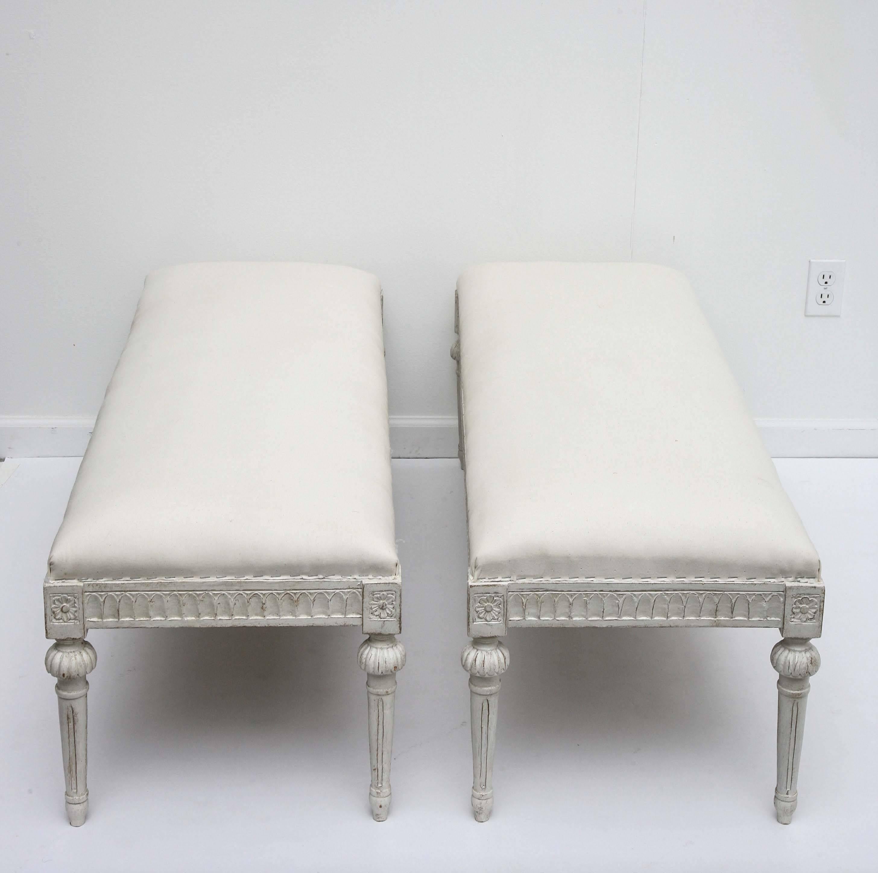A pair of unusual antique Swedish Gustavian painted benches, with carved lambs tongue border on apron, round tapered fluted legs with lovely fluted
round caps on top of legs, carved floral rosettes at top of each leg in the border,
painted in