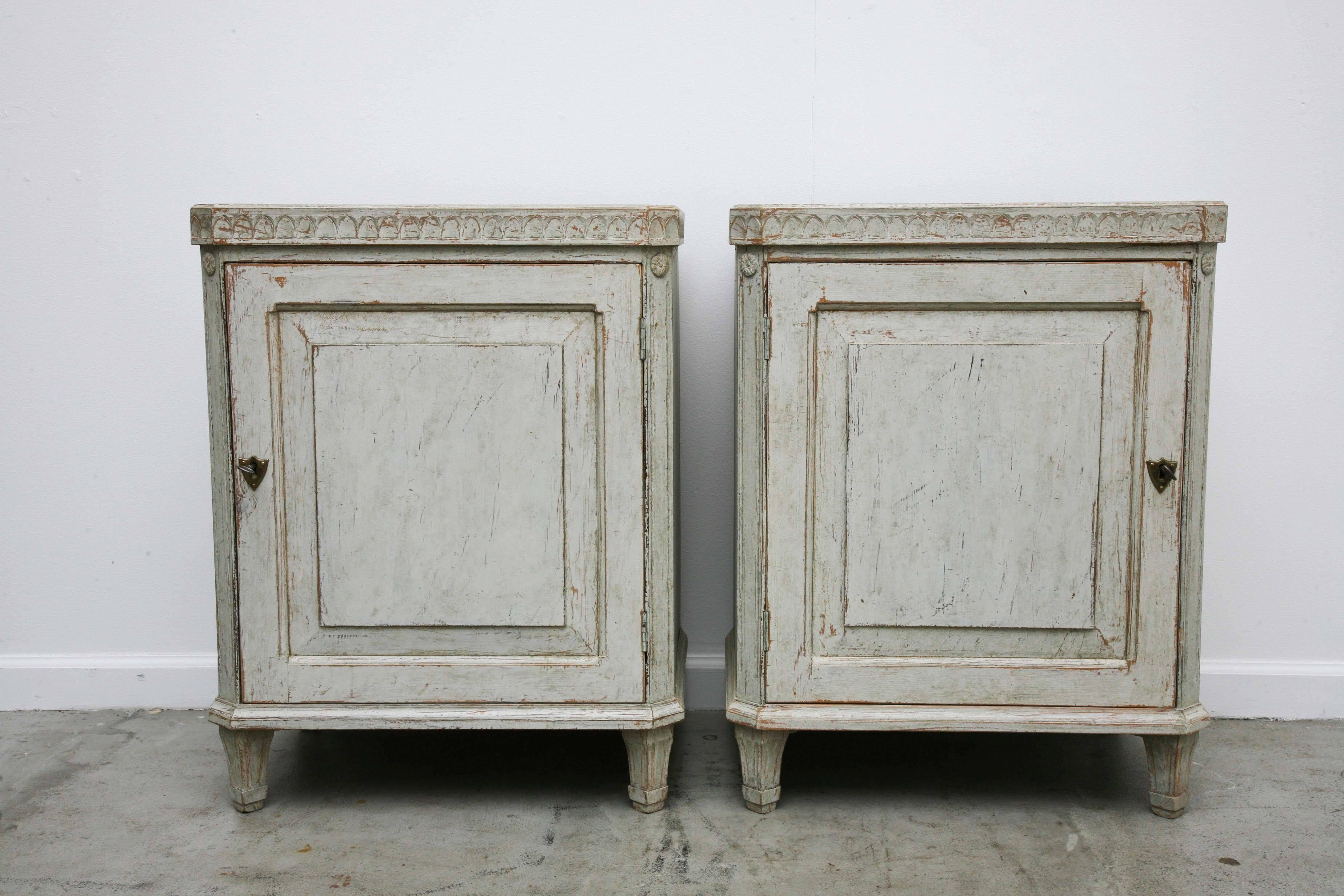 A pair of Swedish antique nightstands, with curved dental molding detail
around top edge, small round floral carving on cut-off fluted corners, with
classic tapering fluted legs, doors with one shelf inside each,
in light green-grey painted