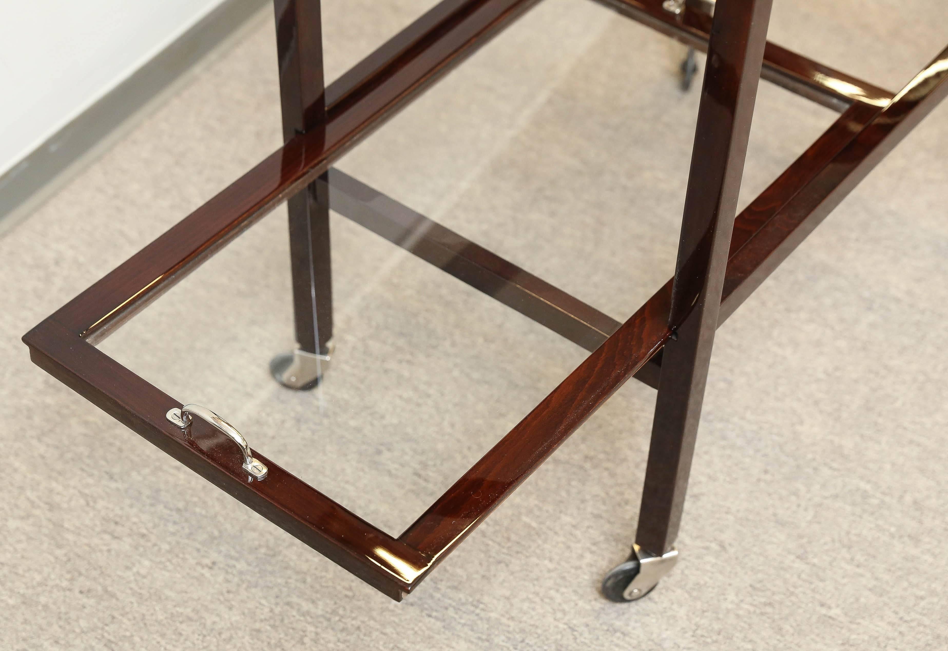 The wooden and chrome frame is attached to the two trays with glass bottom. The bottom tray is removable. It slides out and could be used as a server. There is one handle. Four small wheels are attached to the square shaped legs for an easy