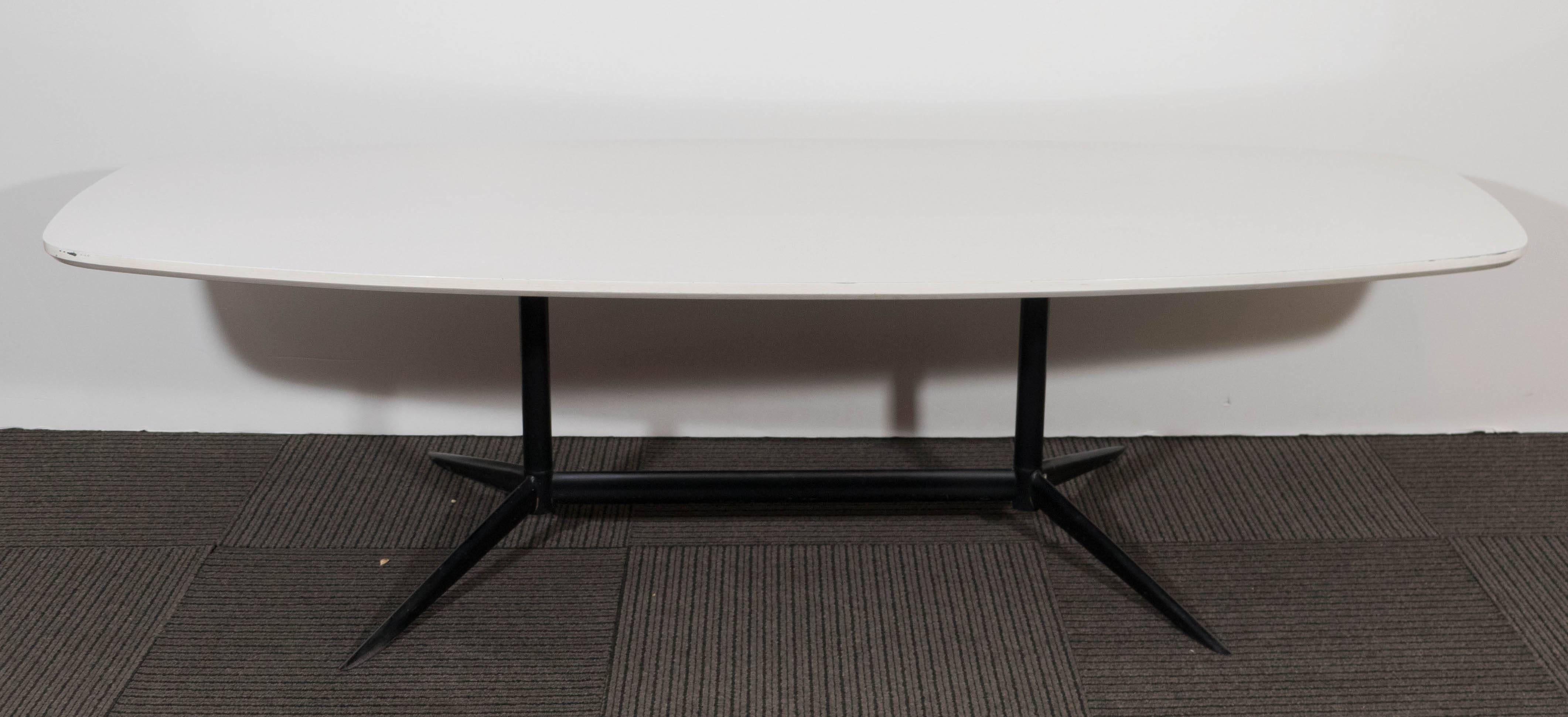 This vintage coffee table, designed in the style of Charles Eames, includes lengthy 'surfboard' style top in white laminated wood, over segmented base in black enameled metal, with sharp tapered legs. Very good condition with minor flaking to top