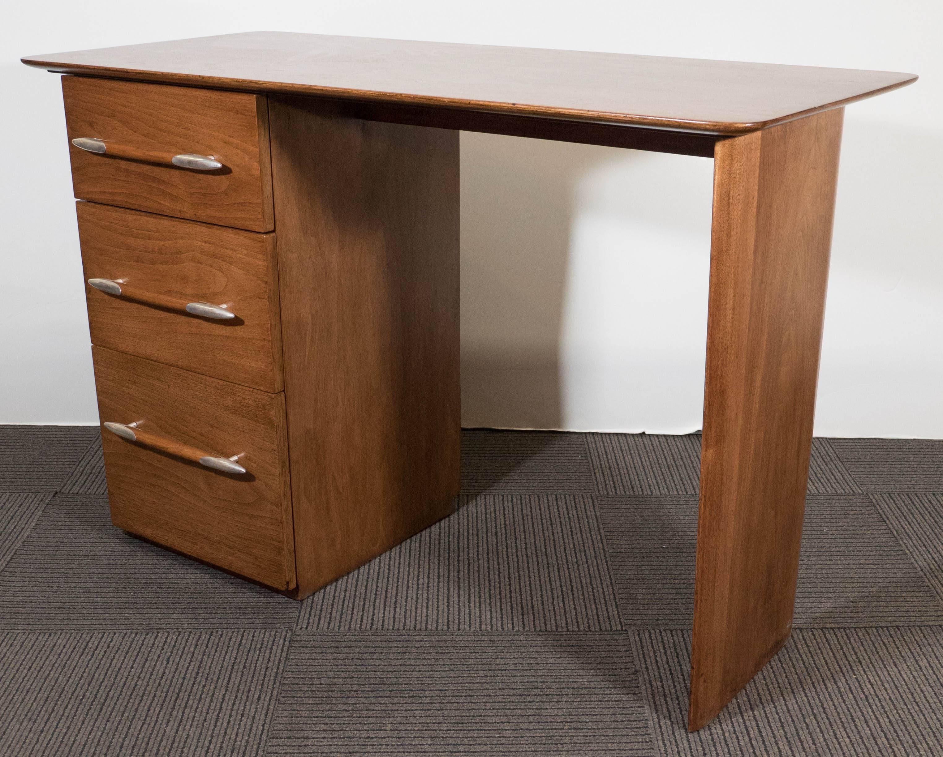 This vintage wooden desk by designer T.H. Robsjohn-Gibbings for Widdicomb Furniture Co., circa 1950s, comes with round cornered table top, above three graduated drawers, each with pull handle, tapered to either end and accented in polished metal