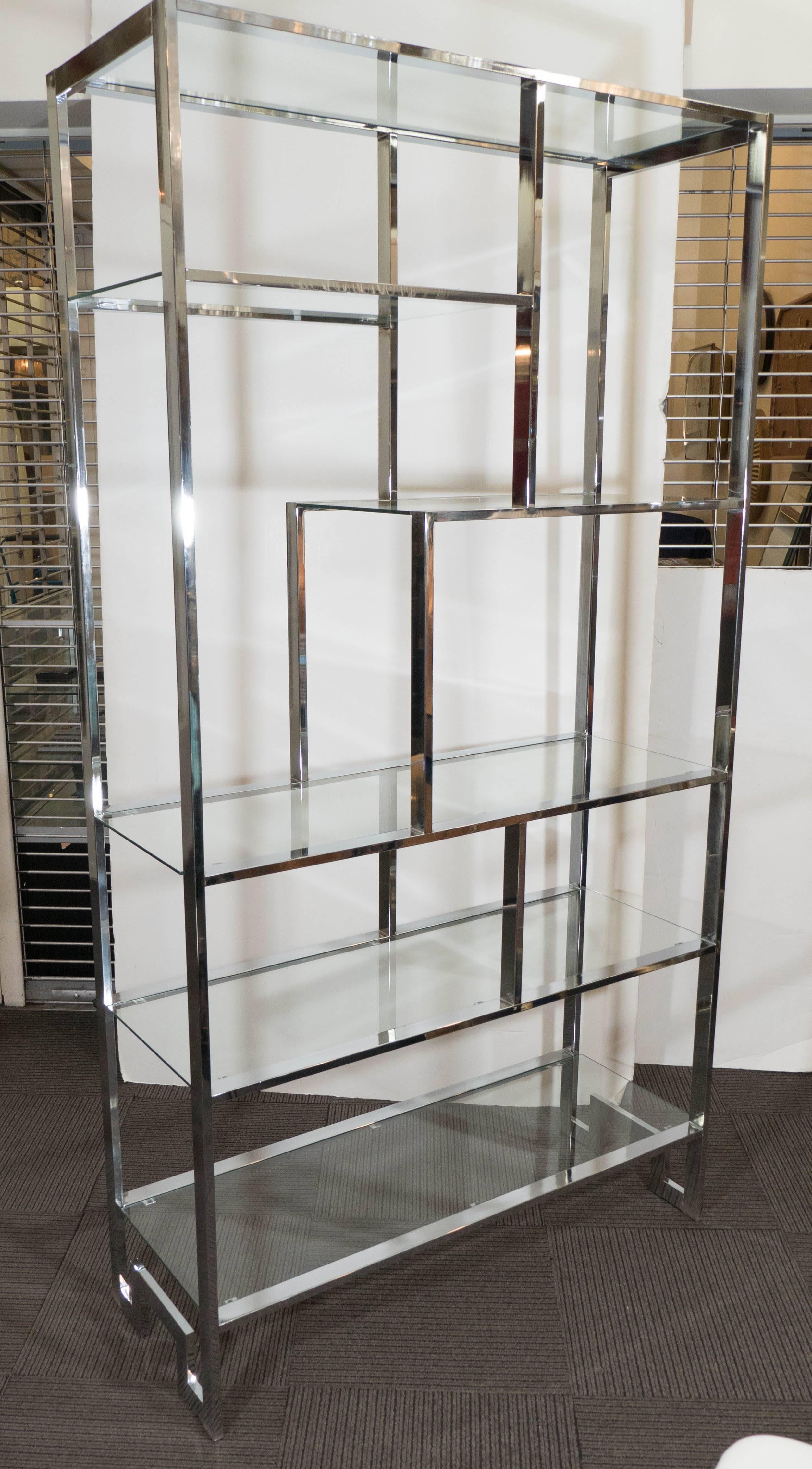 A vintage etagere by designer Milo Baughman and produced circa 1970s, with highly linear polished chrome frame and glass shelves, four full and two short, on Greek key style legs. This unit remains in very good condition, consistent with age and use.