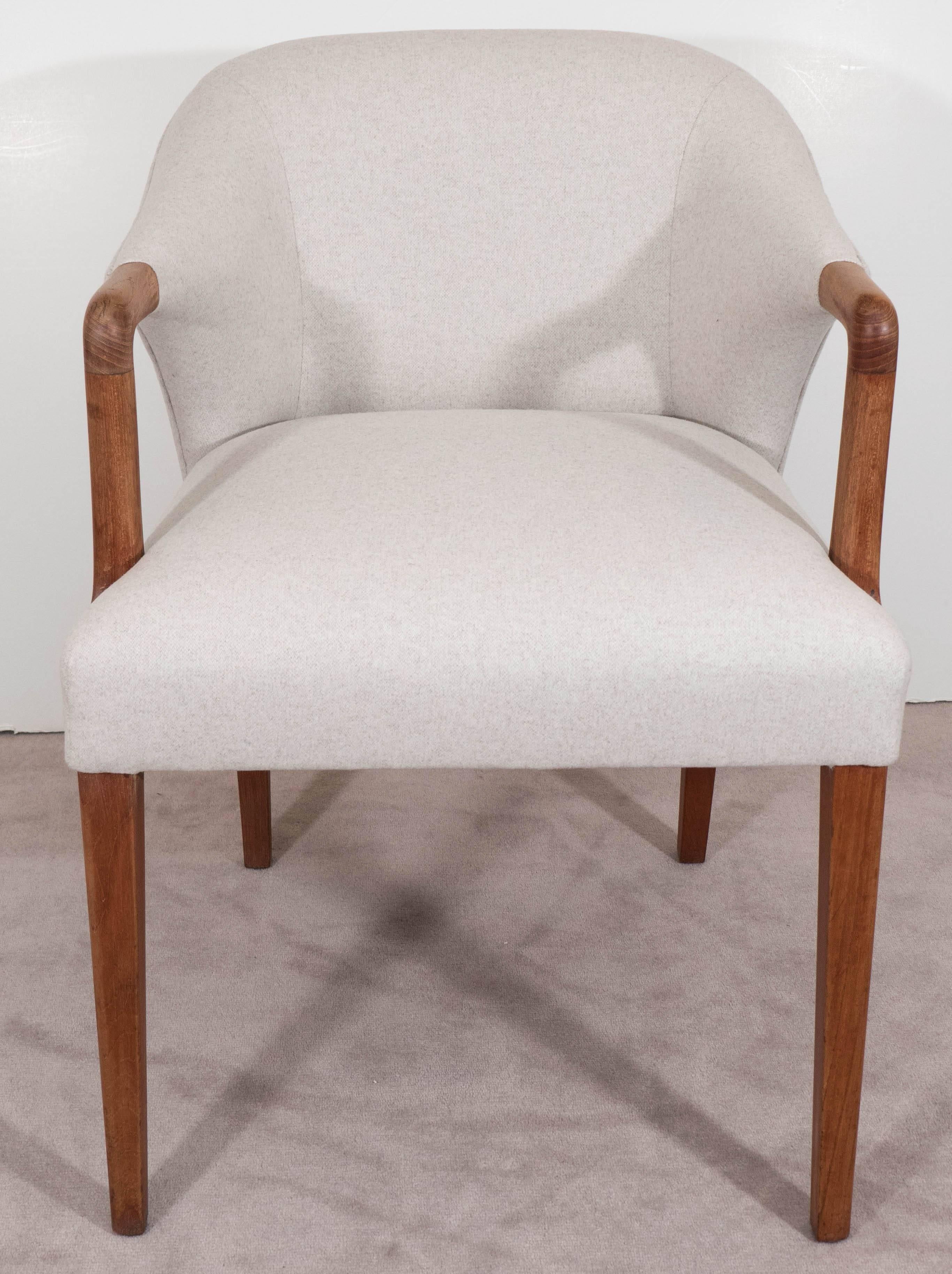A vintage Danish armchair designed in the Scandinavian Modern style, produced circa 1950s to 1960s, with upholstered and cushioned round back and seat, against a teak frame, with gently curved arms on slightly tapered legs. This chair is in