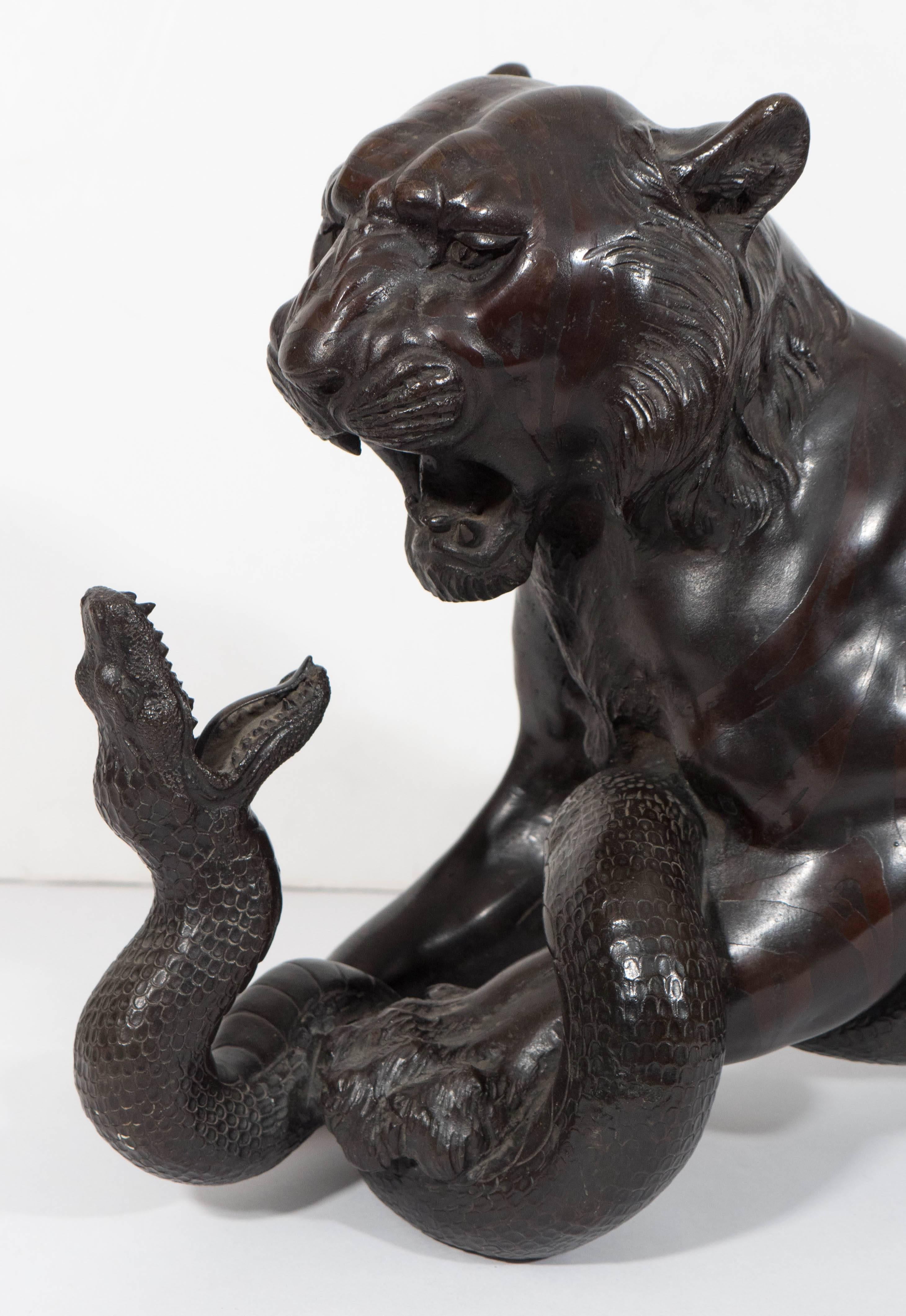 This patinated bronze sculpture, produced in Japan, circa Meiji period, depicts a ferocious tiger and serpent, engaged in deadly combat. The beasts are painstakingly detailed, acid etching stripes applied to the tiger, the snake scales visible along