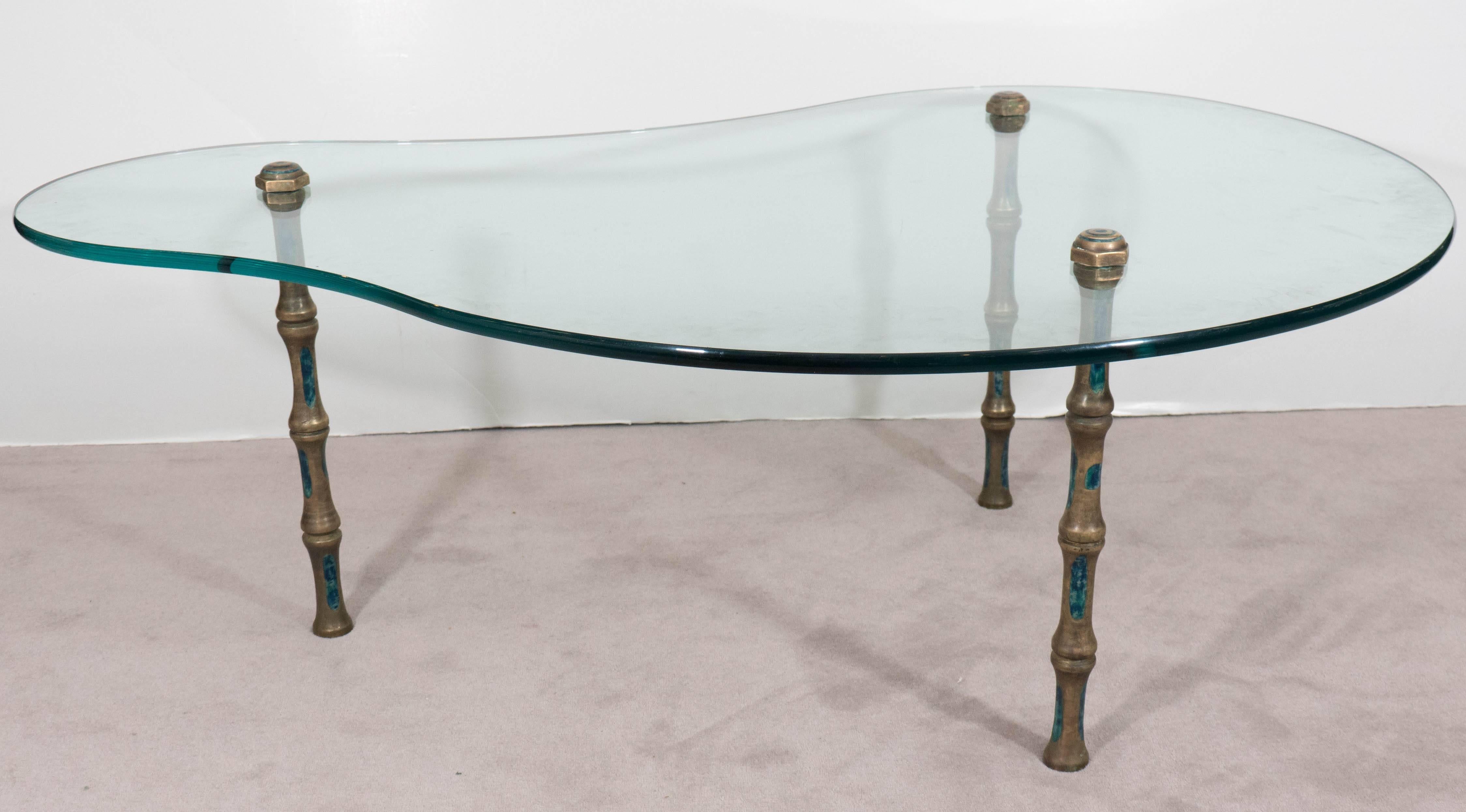 This coffee and cocktail table in the style of Mexican designer Pepe Mendoza, produced circa 1950-1960, includes a biomorphic shaped glass top, mounted on three bronze legs, as faux bamboo stalks, inlaid with enameled turquoise ceramic. Very good