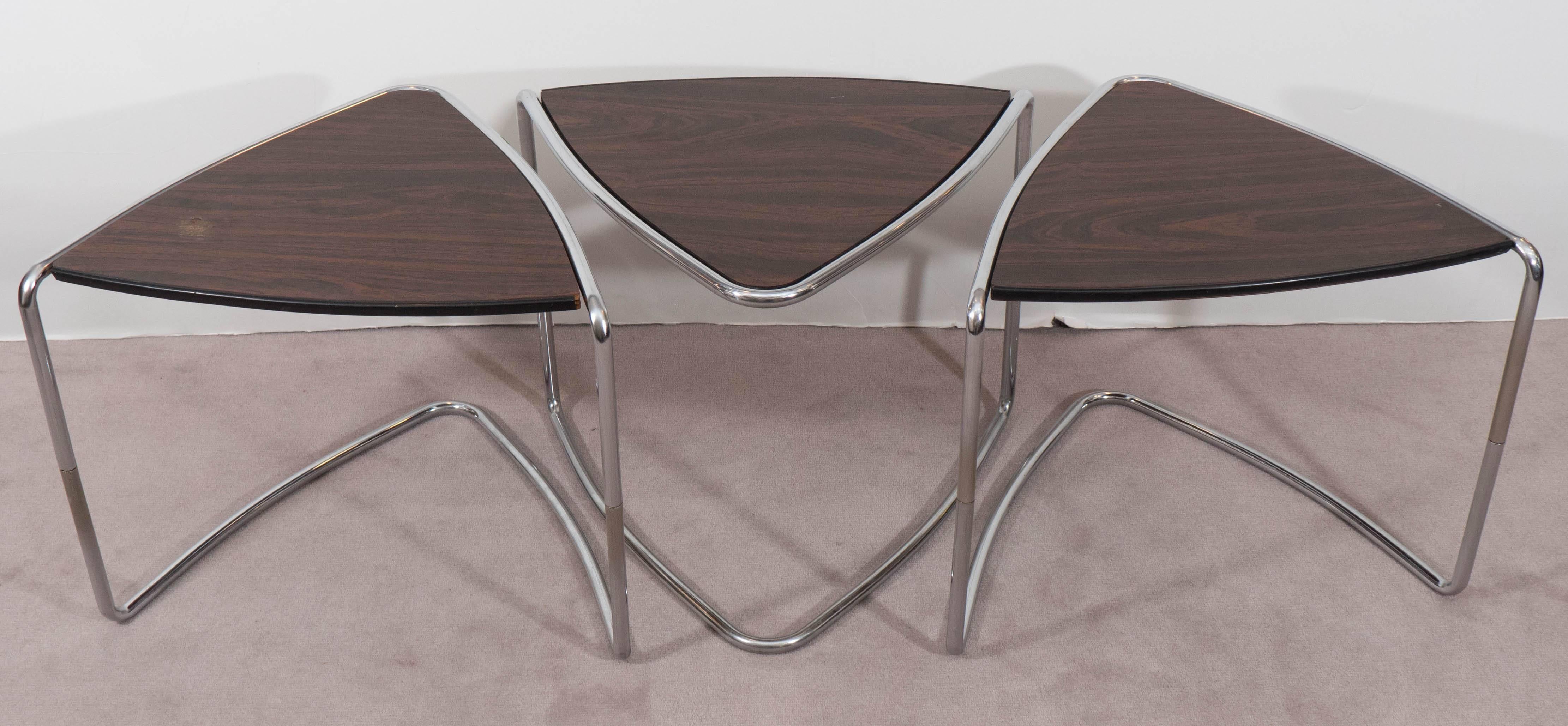 A set of three circa 1970s stacking tables, each with triangle shaped top in laminate wood, against polished chrome, tubular sled base. The tables remain in good vintage condition with age appropriate wear to chrome, including presence of pitting;