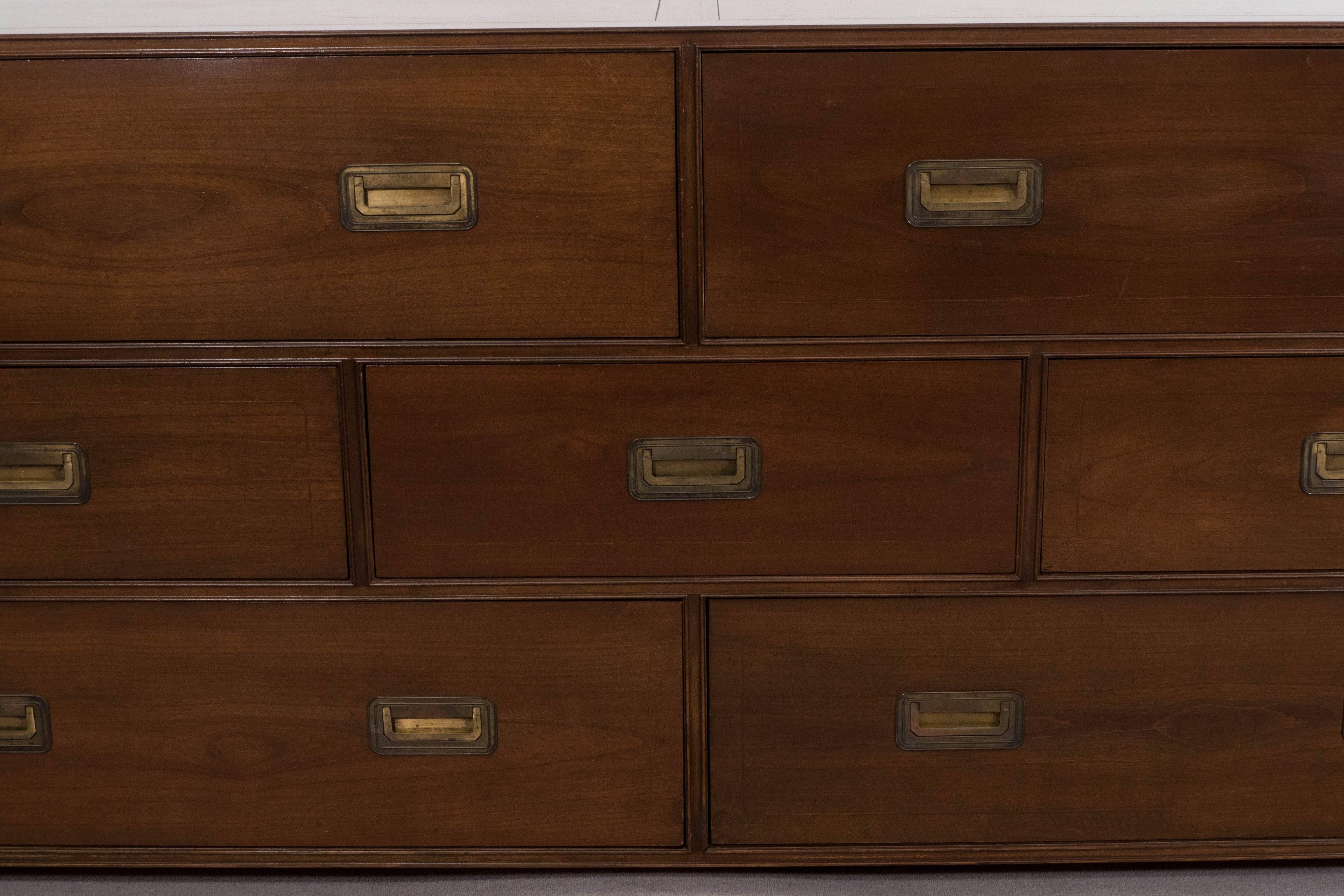 A circa 1970s low chest of drawers and dresser by Baker Furniture Co., entirely in rich toned wood, including seven drawers, four lengthy, surrounding three short at center, each with brass recessed pulls, on bun feet. Markings include the Baker