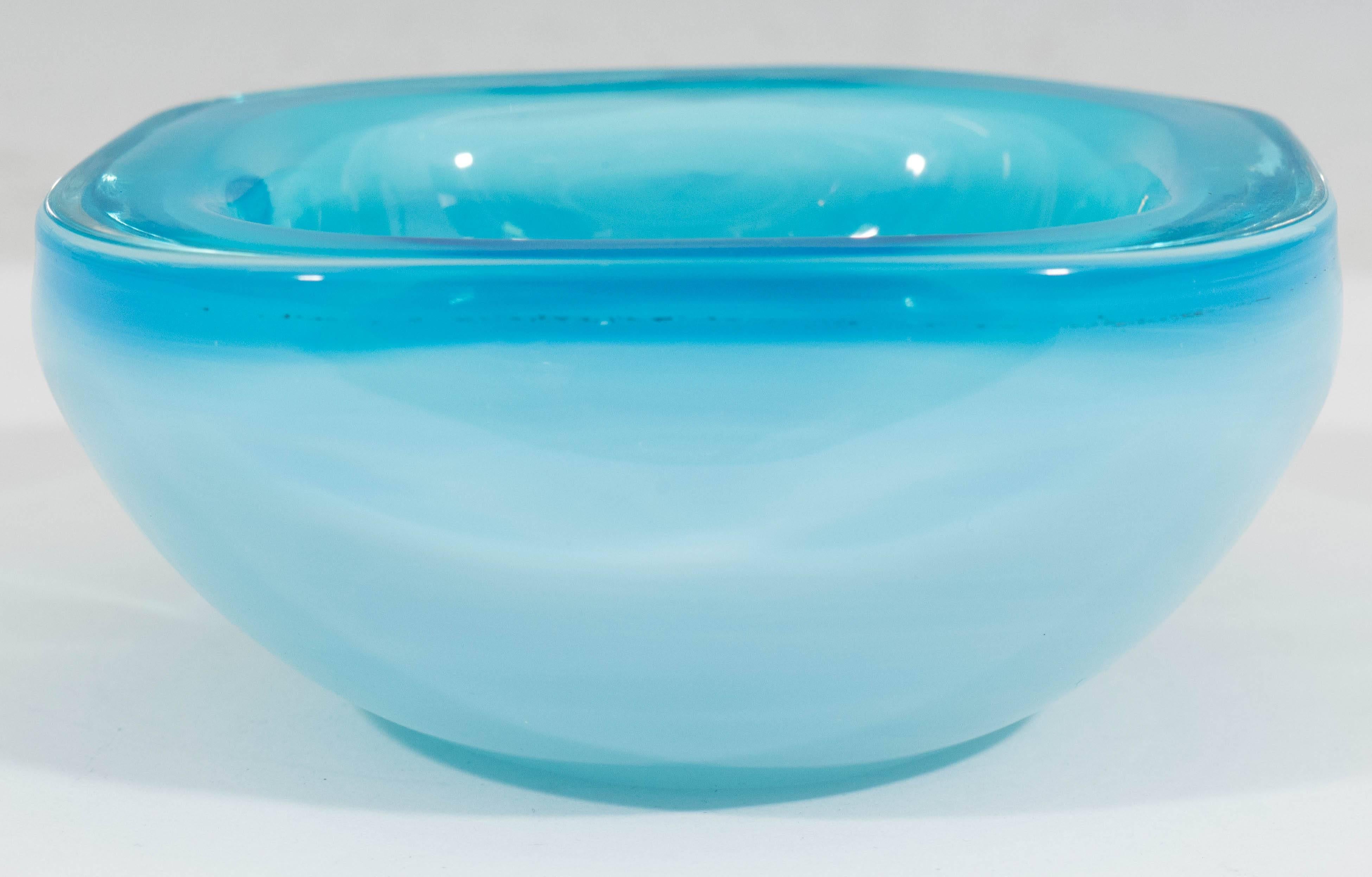 An Italian handblown glass bowl from the Midcentury period, in brilliant blue opaline Murano glass, with thick square shaped corners on a rounded base. Markings include remnants of original label to the bottom. This bowl remains in excellent vintage
