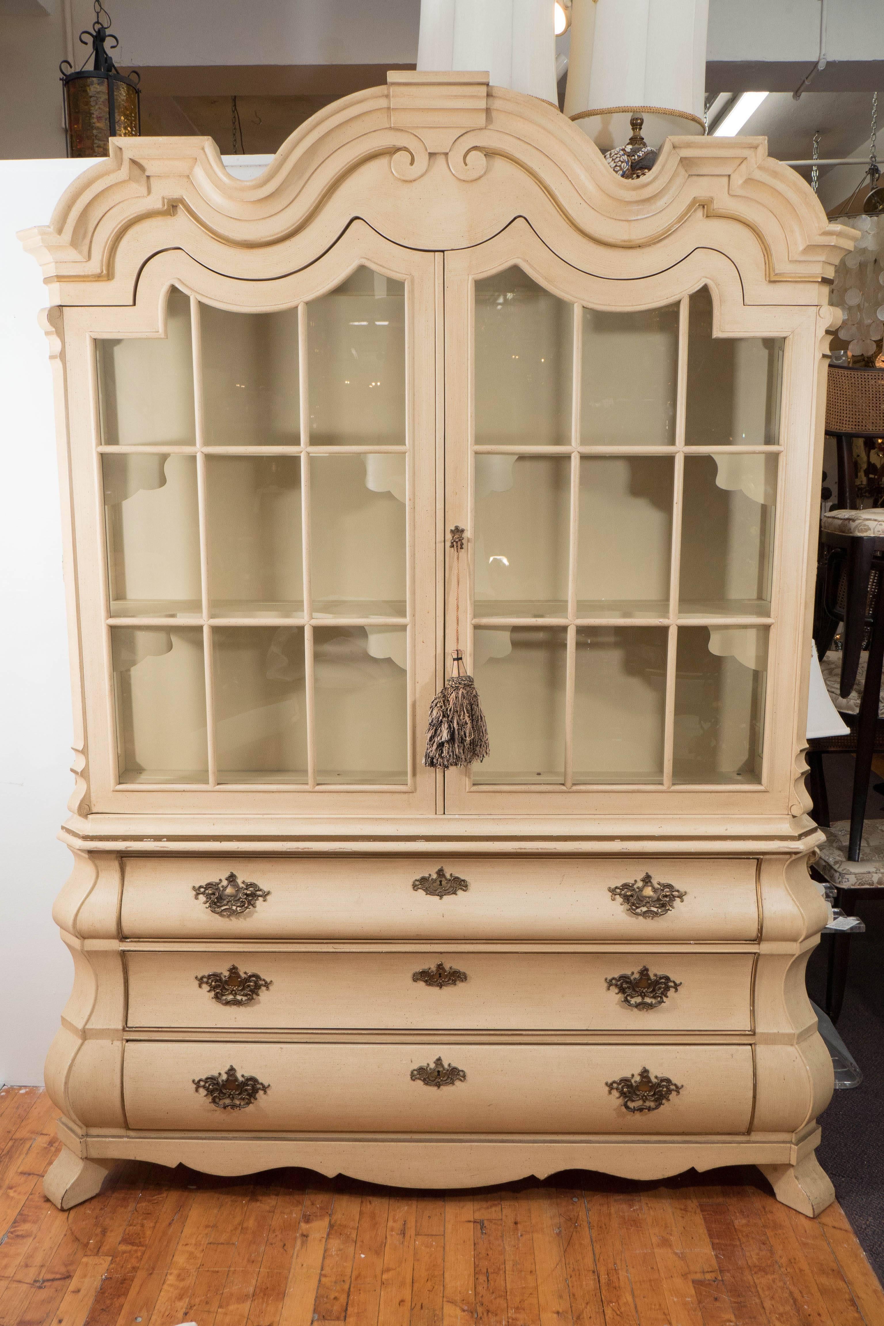 A breakfront cabinet by designer Dorothy Draper from the 'Viennese Collection,' produced, circa 1960s by Henredon, with curved pediment on glass display, inset with two long shelves, above three graduated bombé form drawers, with elaborate acanthus