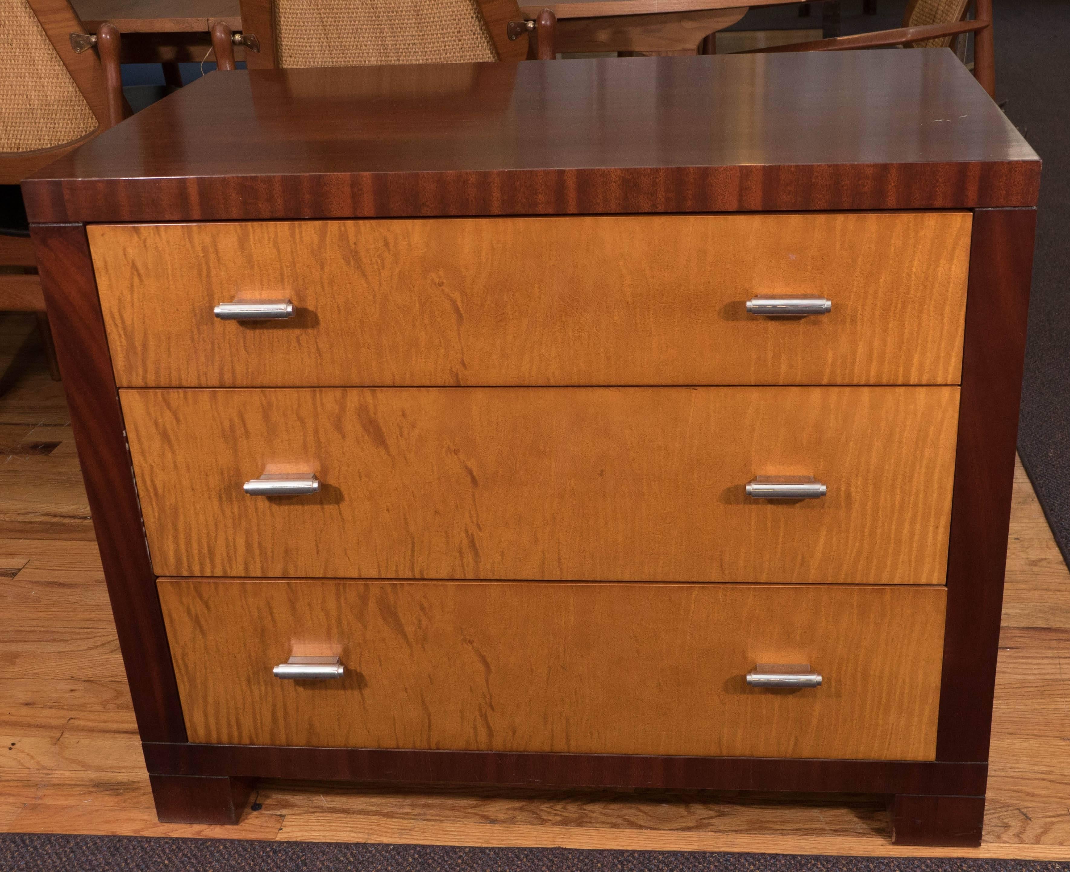 This dresser and commode by John Widdicomb comes with three drawers, each with bright sycamore fronts and two cylindrical pulls in nickel, against a linear rich mahogany frame, on block feet. Markings include makers label [JW/John Widdicomb] to the
