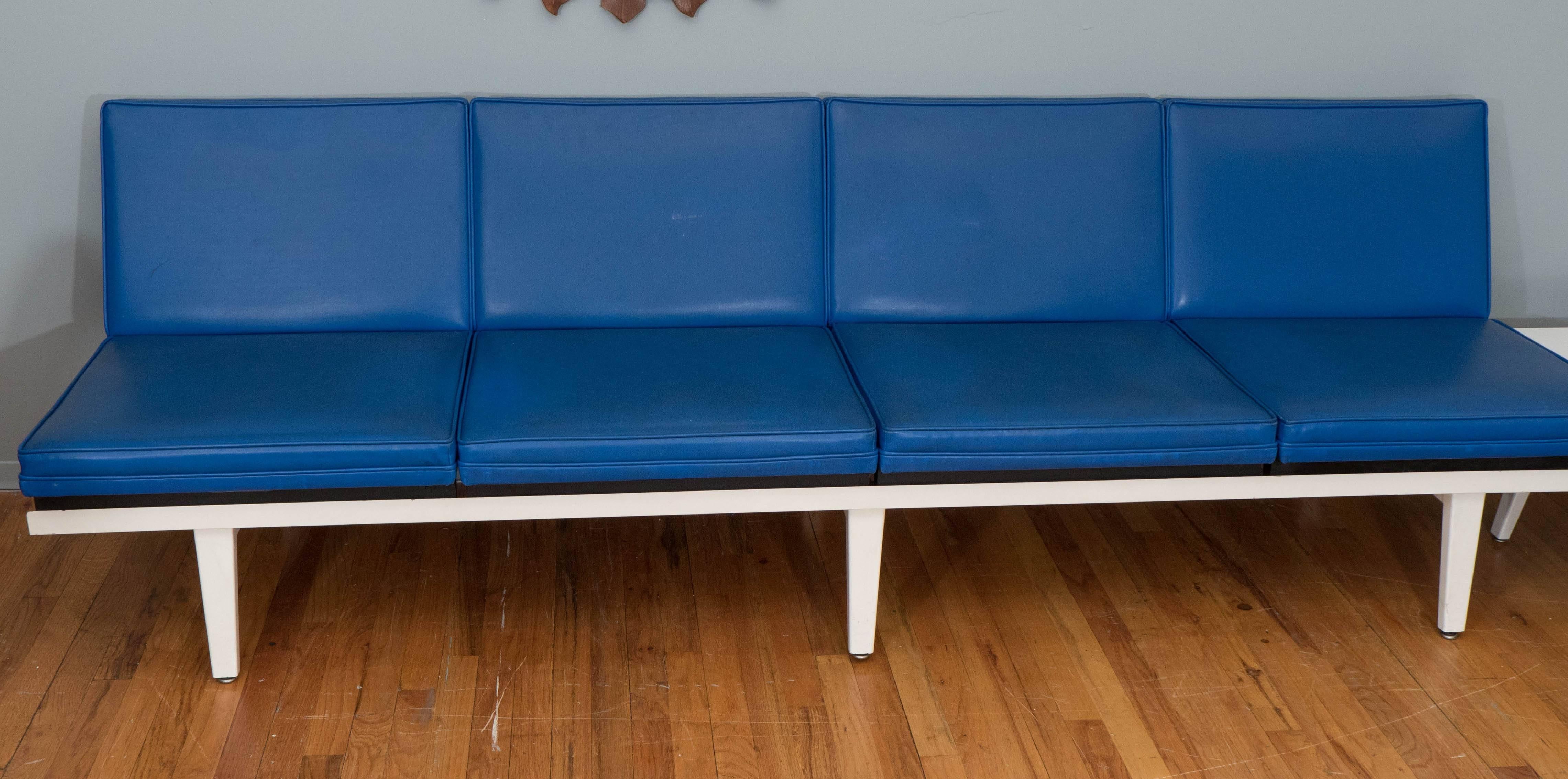 A 1960s sectional living room set by designer George Nelson for Herman Miller, which includes a four seat sofa and two seat bench, upholstered in blue vinyl cushions, against a white enameled metal frame, with attached side table. Very good vintage