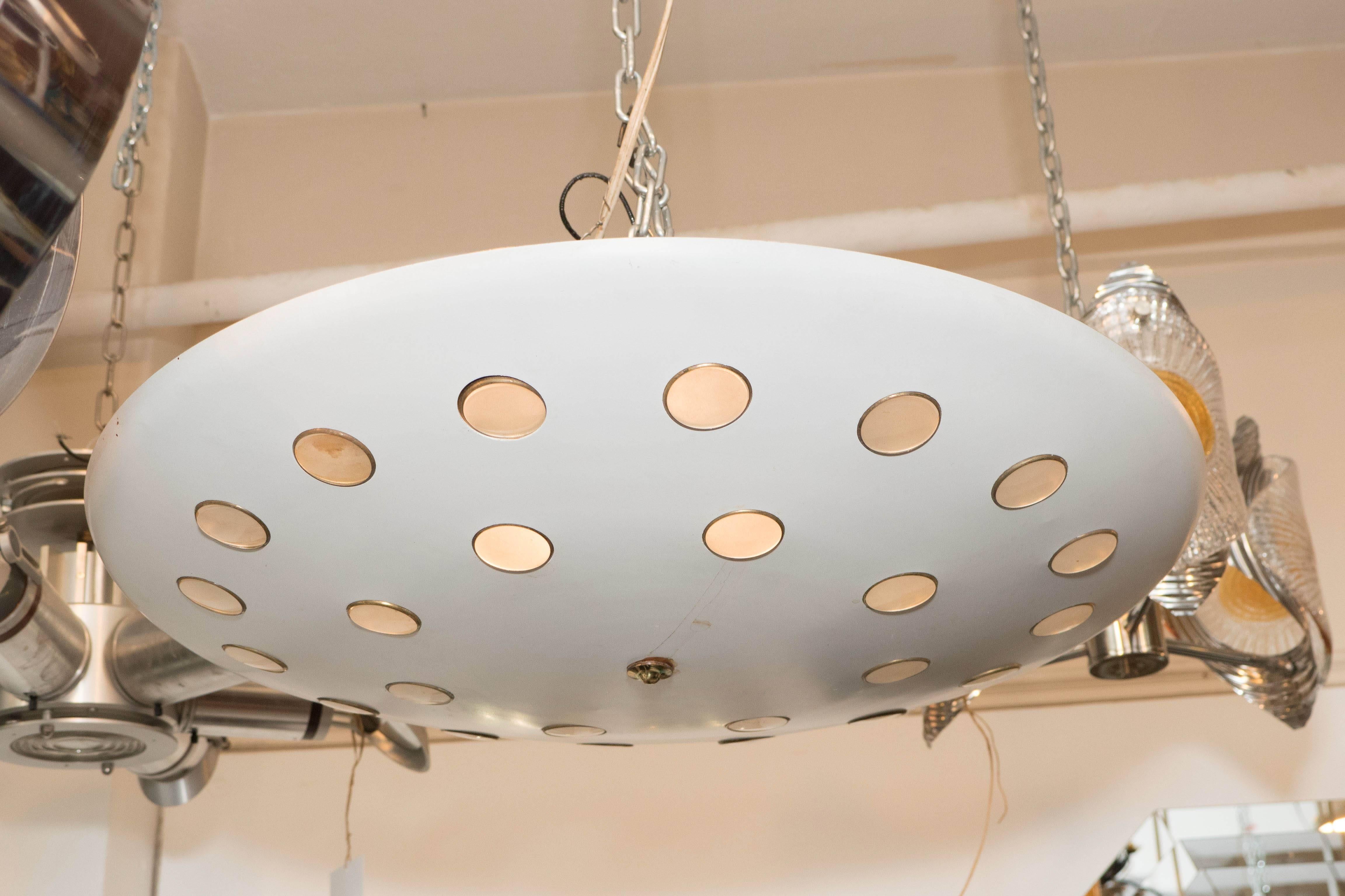 A vintage, highly modern ceiling lamp in the style of Emil Stejnar, produced circa 1960s, with white saucer shade in enameled metal, detailed with brass lined perforated holes, each with lens, suspended from conical canopy. This light fixture