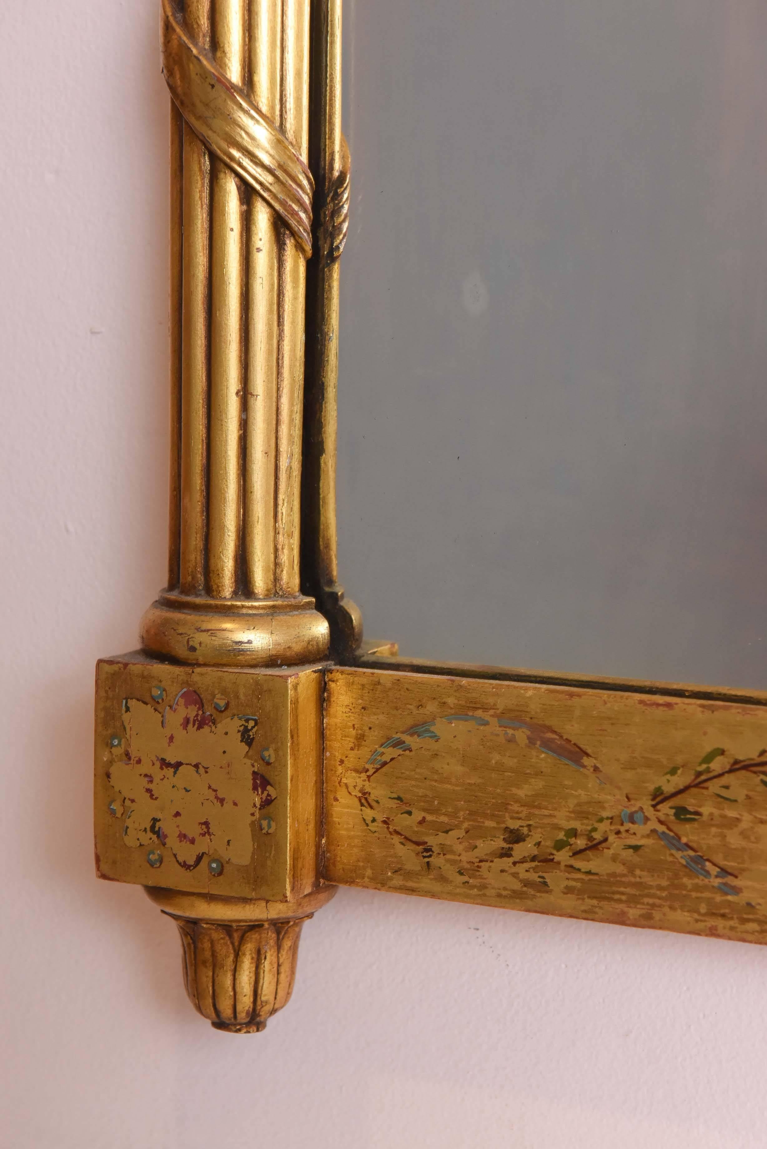 A lovely giltwood mirror with hand-painted floral swag motif and framed by beautiful columns with an urn finial at its top. A very nice size with great detail to the overall carved giltwood frame. Retaining most of its original polychrome painting