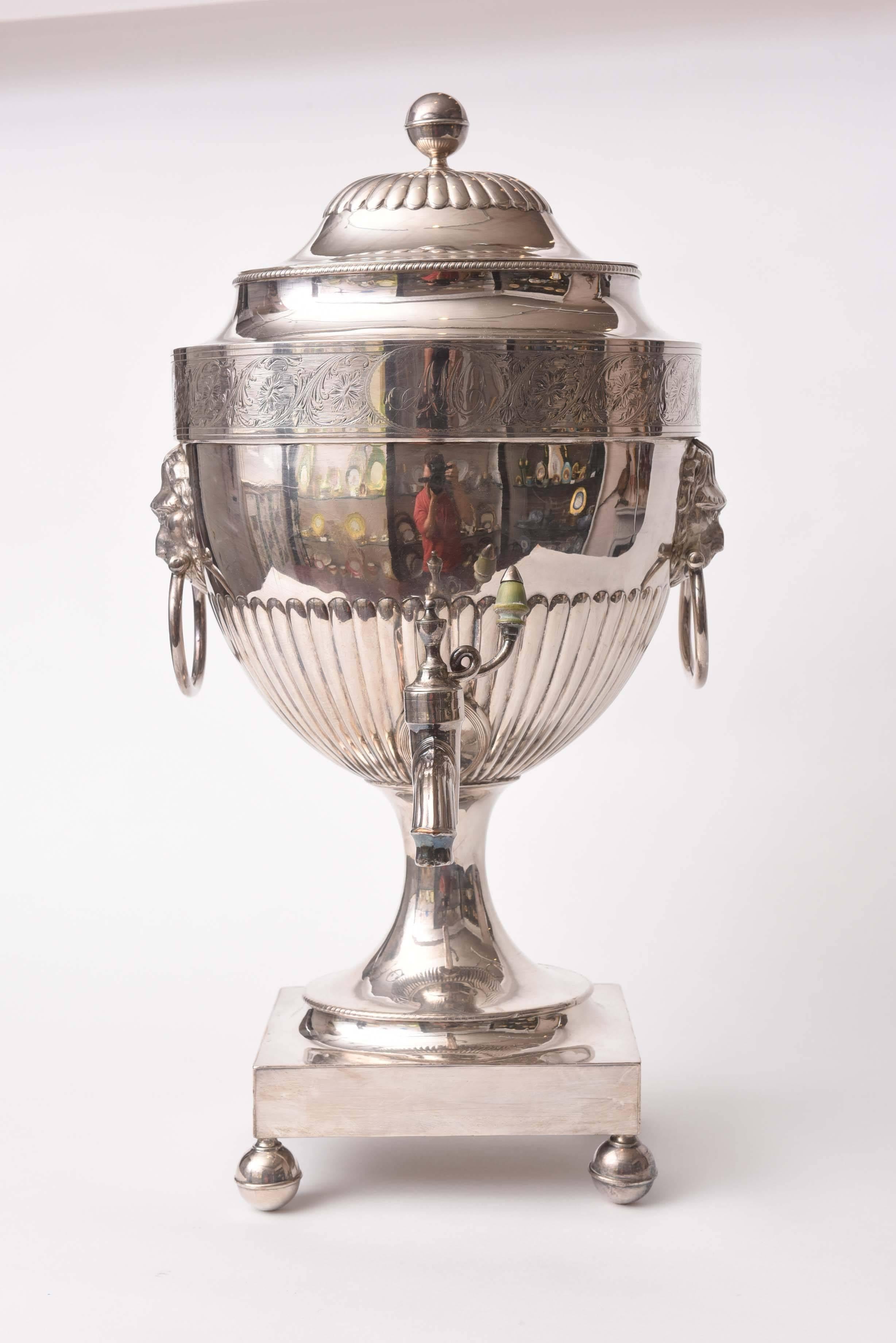 An impressive and highly decorative silver plated hot water, tea or coffee urn. We attribute to one of the Sheffield England manufacturers and note the Classic lion's head handles, ball feet, urn shape and finial for this attribution. There is only
