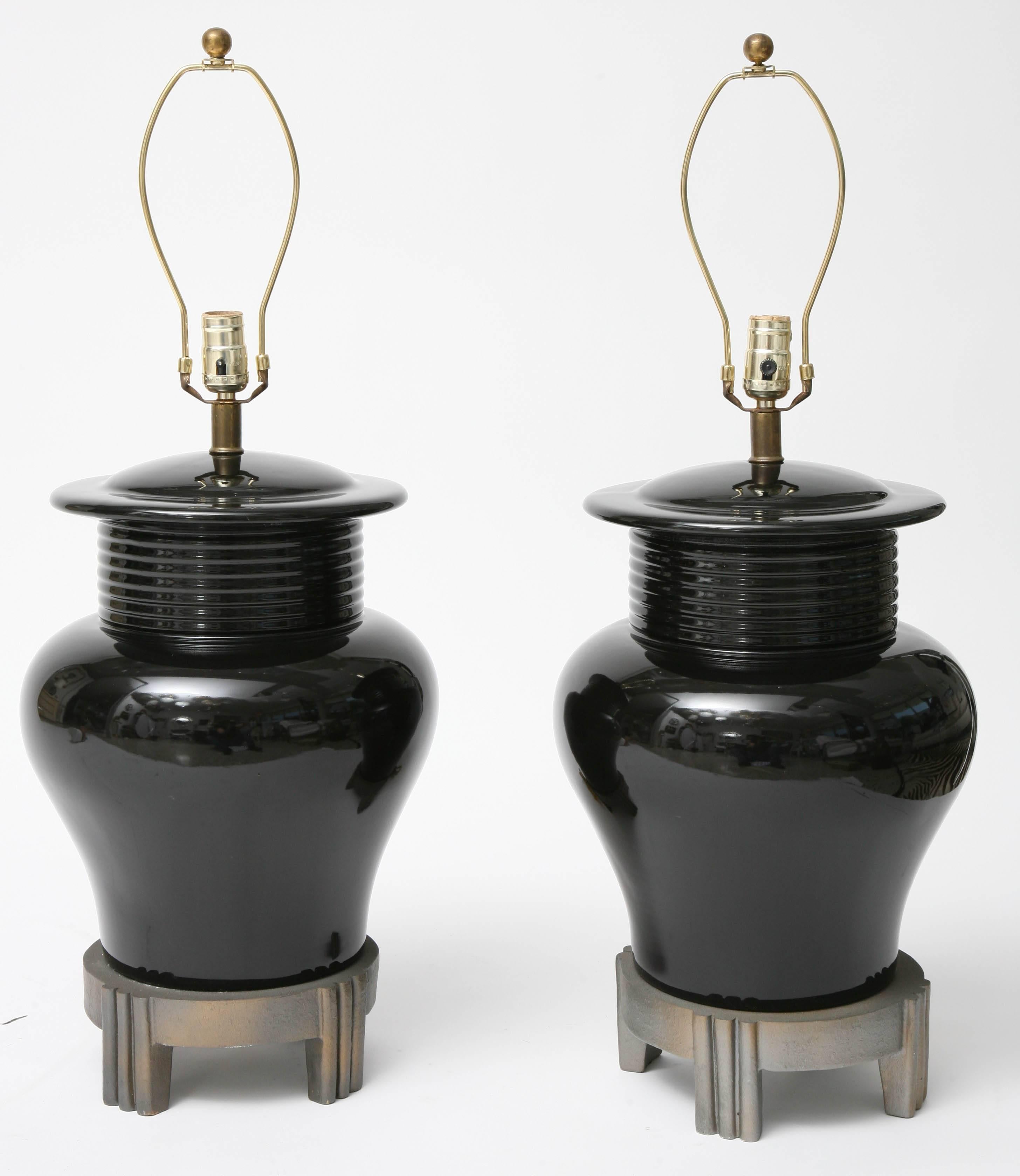 This handsome pair of table lamps are in the Art Deco taste with Asian influence in their form and size. The vase form is of ceramic in a high-gloss black color and the bases are a composition with a grey-tone finish and color.

Note: The lamps