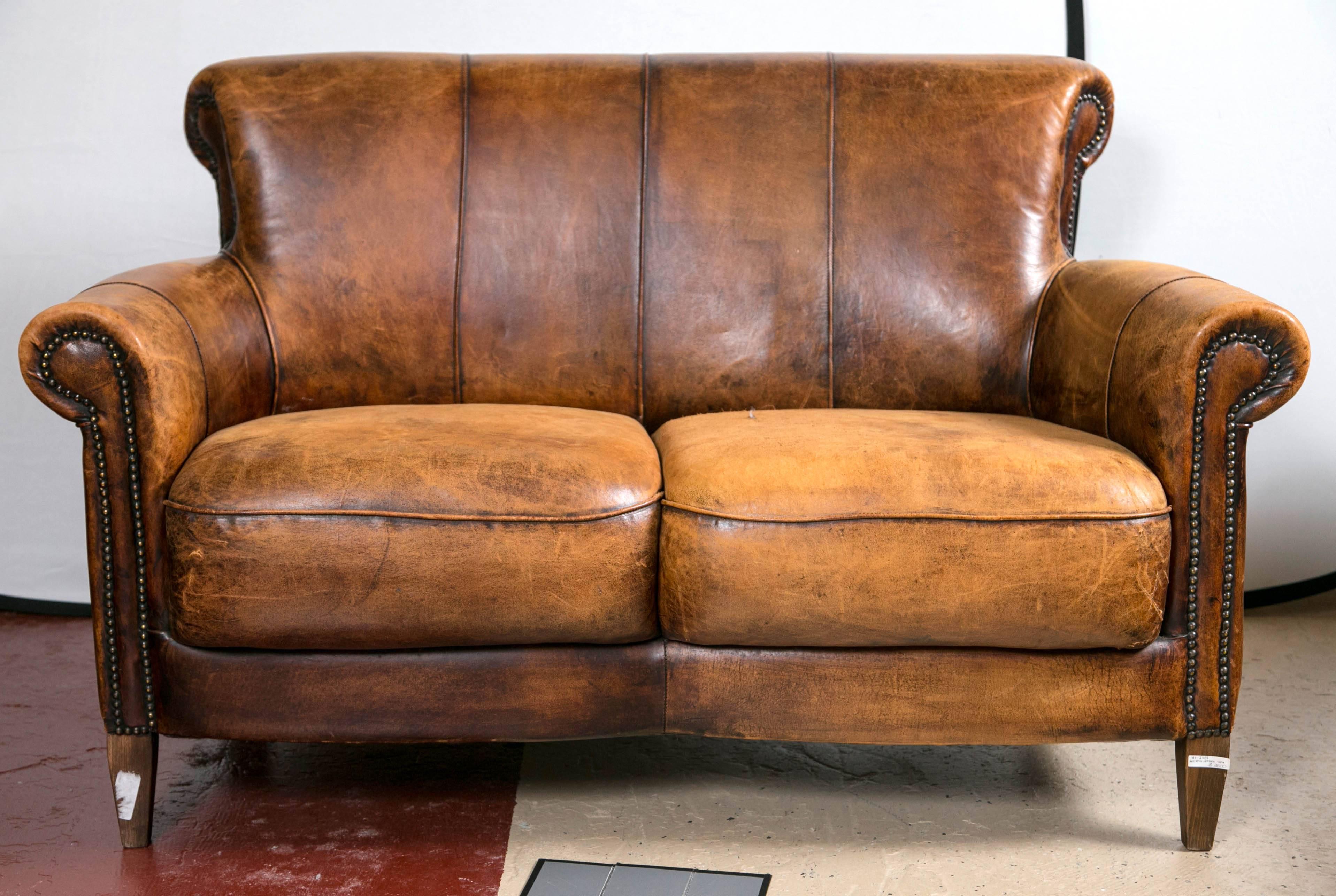 A vintage French distressed Art Deco leather sofa. A fine constructed worn leather settee in the deco taste with carved arms and tack decorated fronts.

Seat height: 18