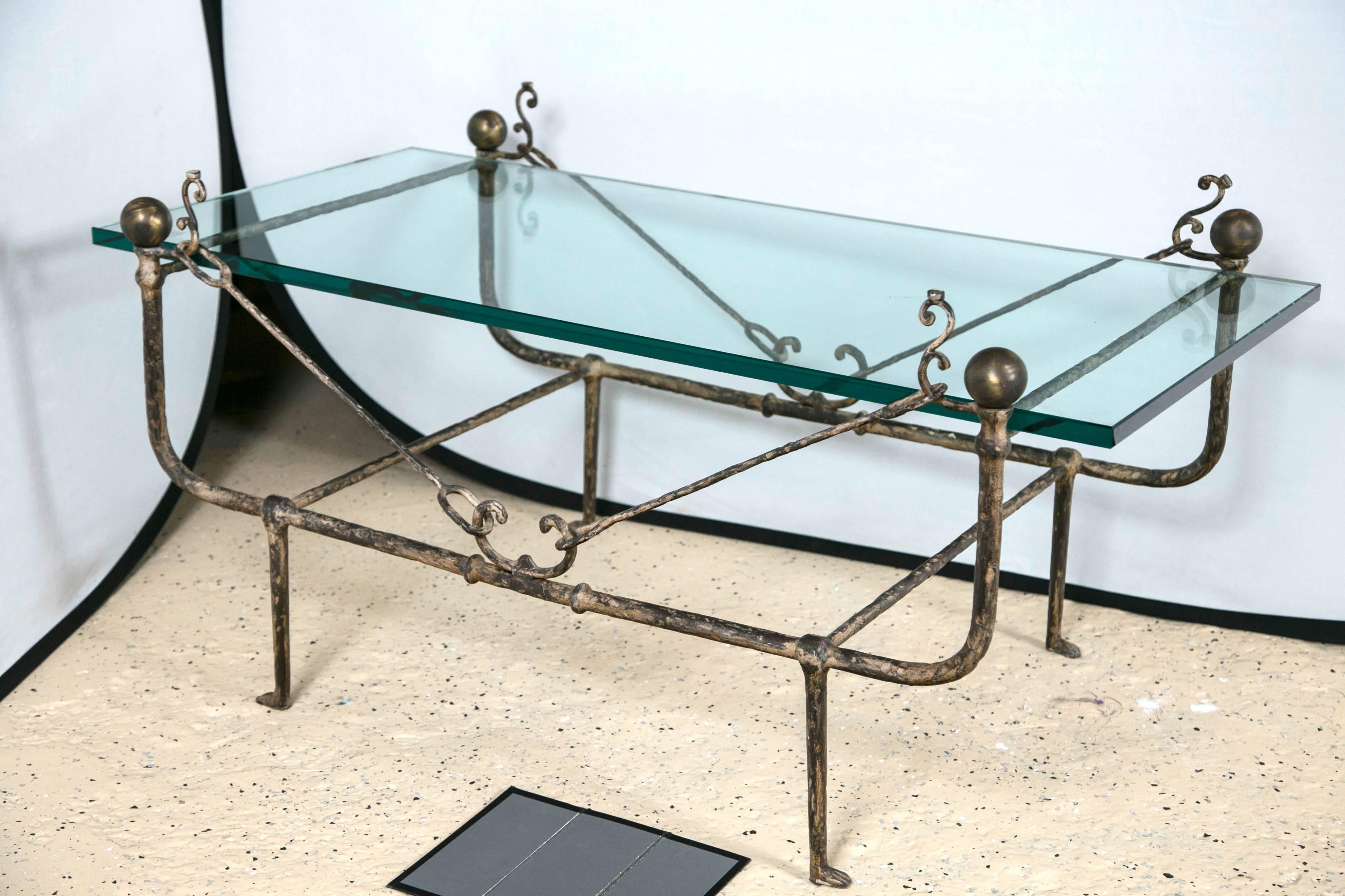 A Diego Giacometti style glass top coffee low table. The iron base with undercarriage and paw feet having sleek and elegant lines terminating in round pediments. The whole supporting a think glass top of rectangular form.