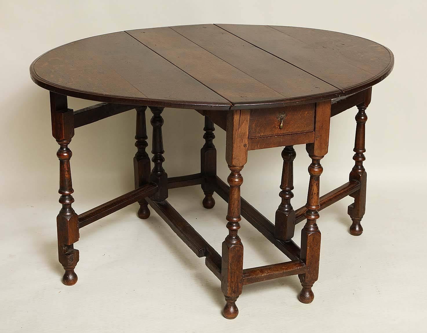 An early 18th century English oak gateleg table, the oval top with shallow ogee edge, the base with single drawer over balustrade turned legs with original bun feet and joined by molded stretcher, the whole with even mellow dark color.  The gateleg