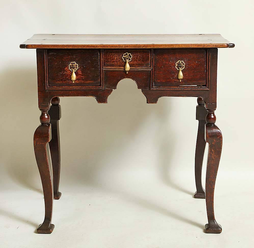A finely made English 18th century country side table, or lowboy, in the formal manner having reentrant corners to the top over three molded drawers above scalloped apron, standing on unusual cabriole legs beginning with a turned ball over a square