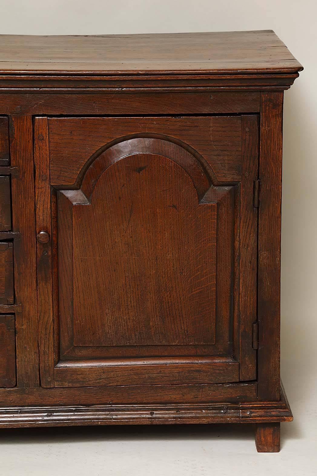 18th century Welsh oak cabinet form low dresser, the molded top over two tombstone panel doors flanking flight of four graduated drawers having mahogany banding, standing on molded base supported by original stile feet, the whole with good rich