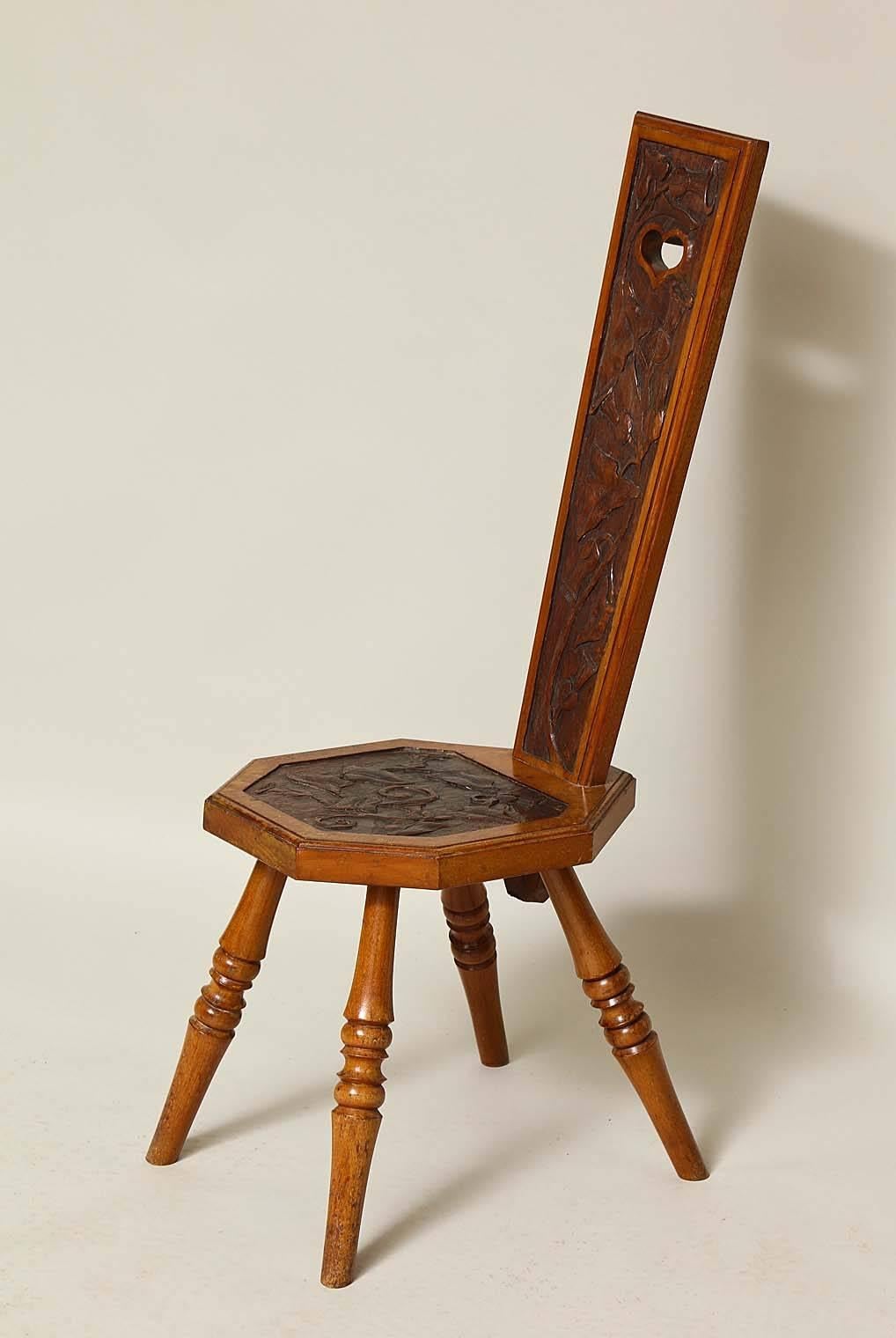 Amusing English Arts and Crafts fireside chair with heart cut-out handle, morning glory vine carved narrow tapering back over similarly carved octagonal seat standing on turned splayed legs, the whole with good patination and characterful style.