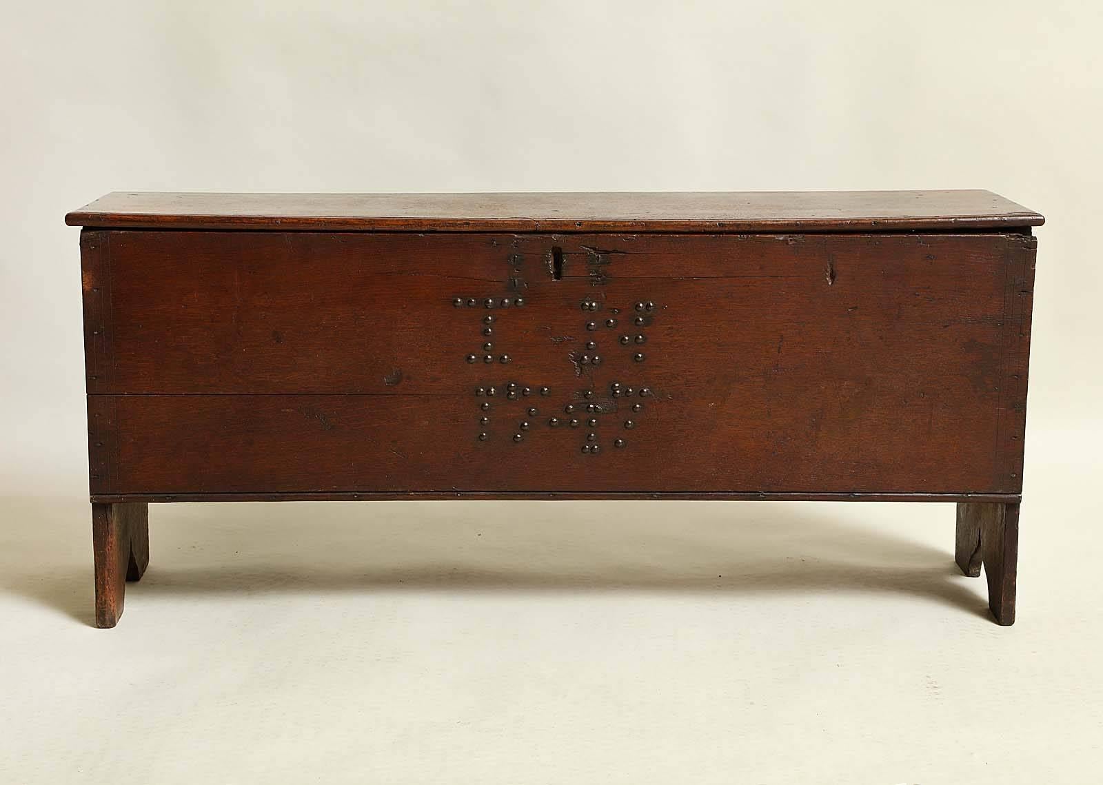 Good 18th century English oak six plank chest, the simple top with original iron strap hinges and lock hasp over bootjack sides having arched feet and scroll carving, the front decorated with brass tacks forming the date of 1747.
