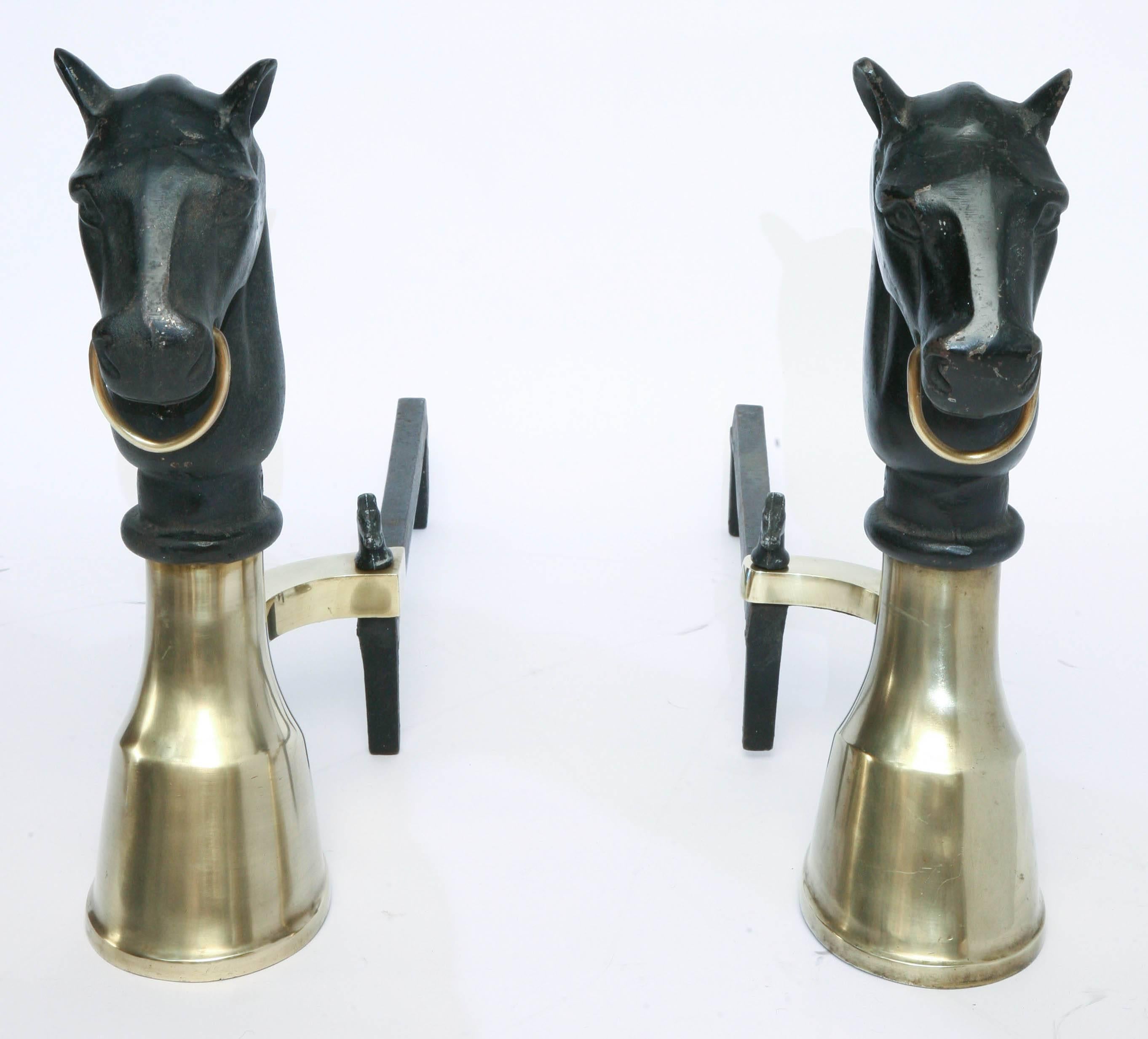 Handsome pair of equestrian andirons consisting of a black iron horse head on a solid brass hoof and having iron horse head finials at base.