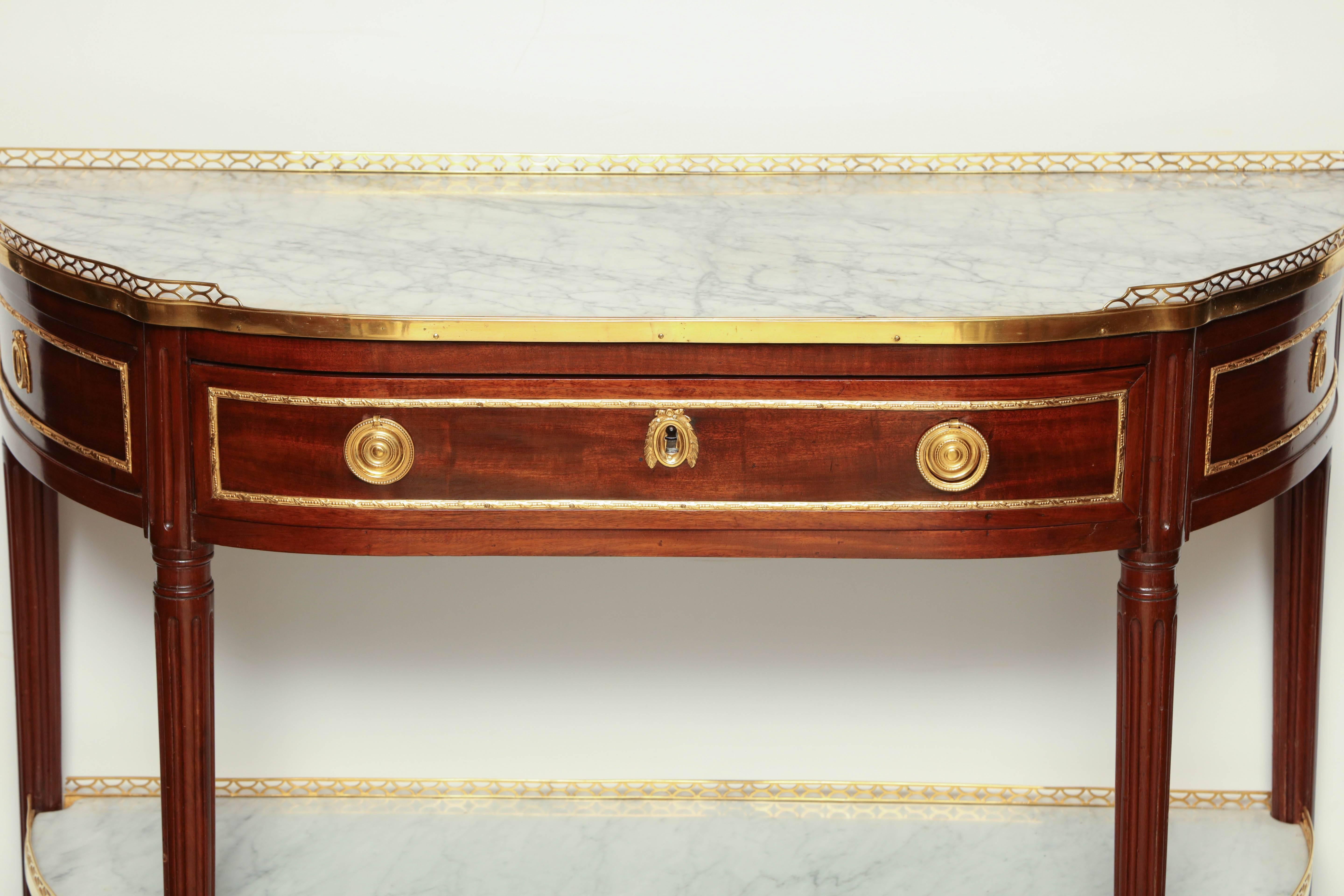 A fine French Louis XVI marble top mahogany demilune console dessérte. With pierced bronze gallery, frieze drawer and marble top shelf stretcher base.