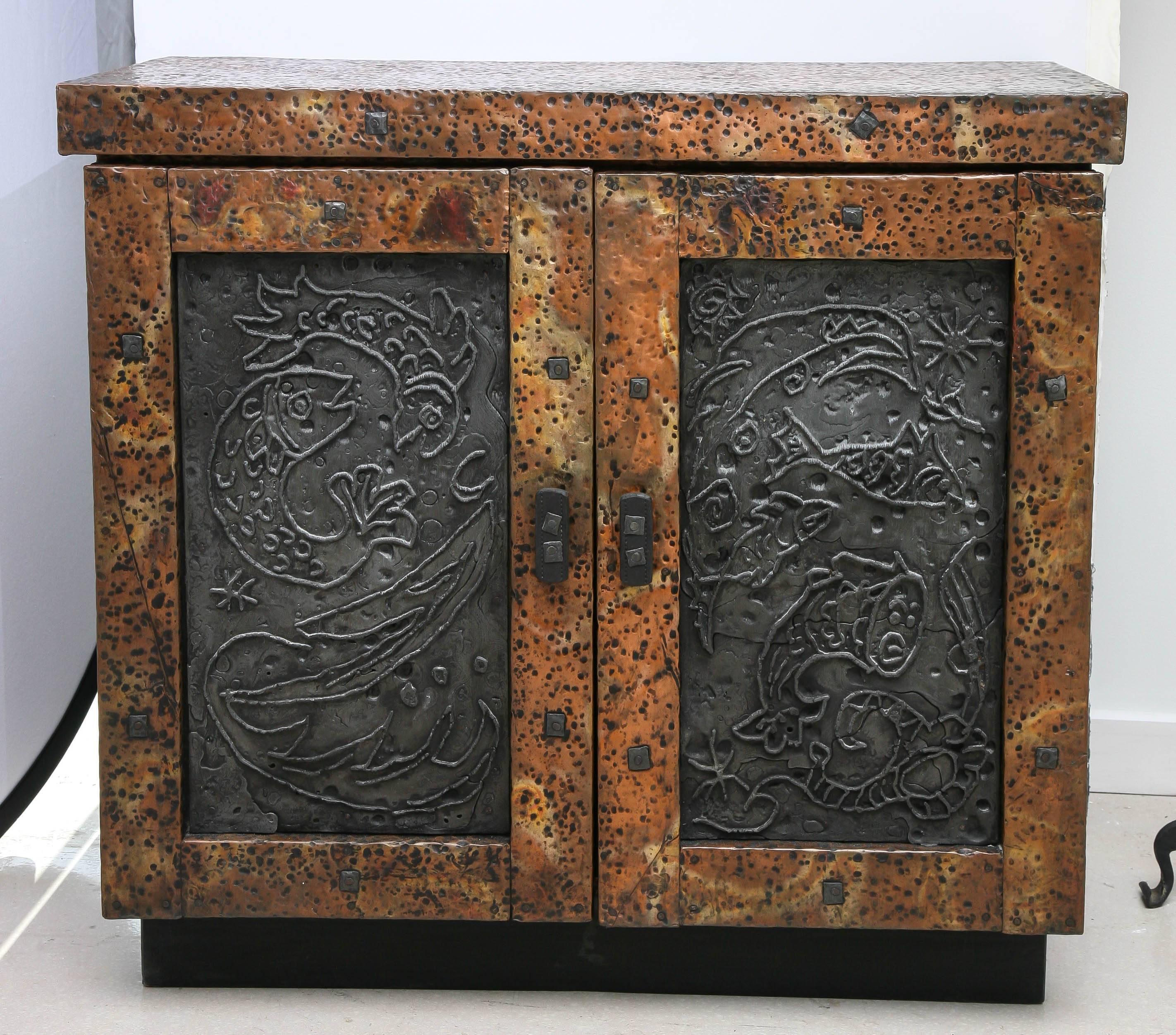 Vintage mixed metal hammered cabinet by the Arenson studio- a father and son duo active in Florida in the 1970s. The Brutalist cabinet has double doors which open to reveal a single shelf. The piece is signed.