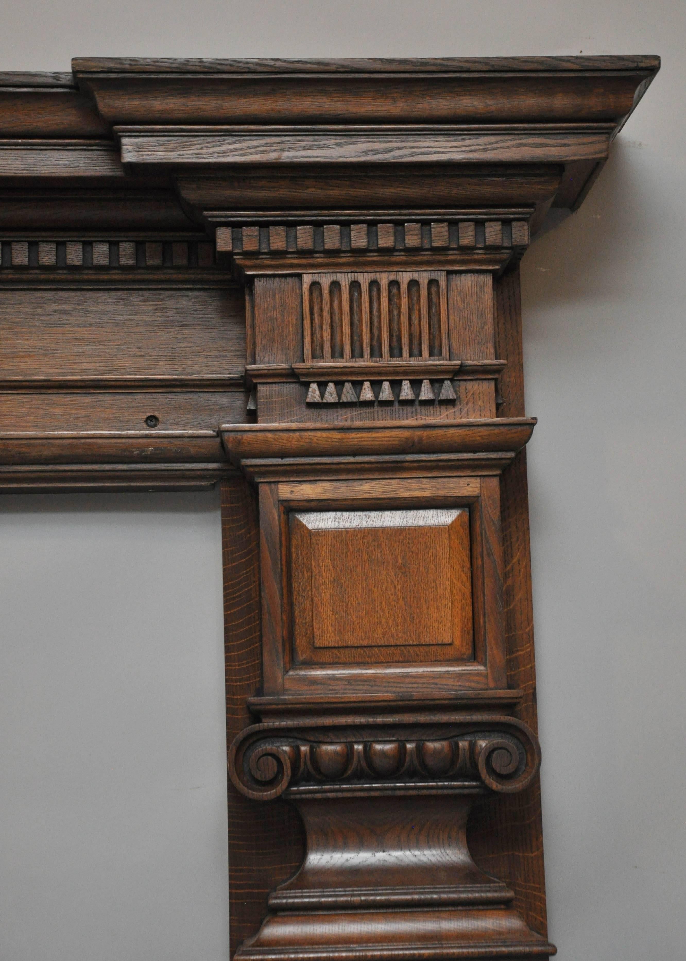 19th Century Palatial English oak fireplace mantel in the tudor style. Shapely top surface above a a stepped recessed frieze with dental detail trim; on either side of freize panel is a square recessed block above an Ionic columns, cap with