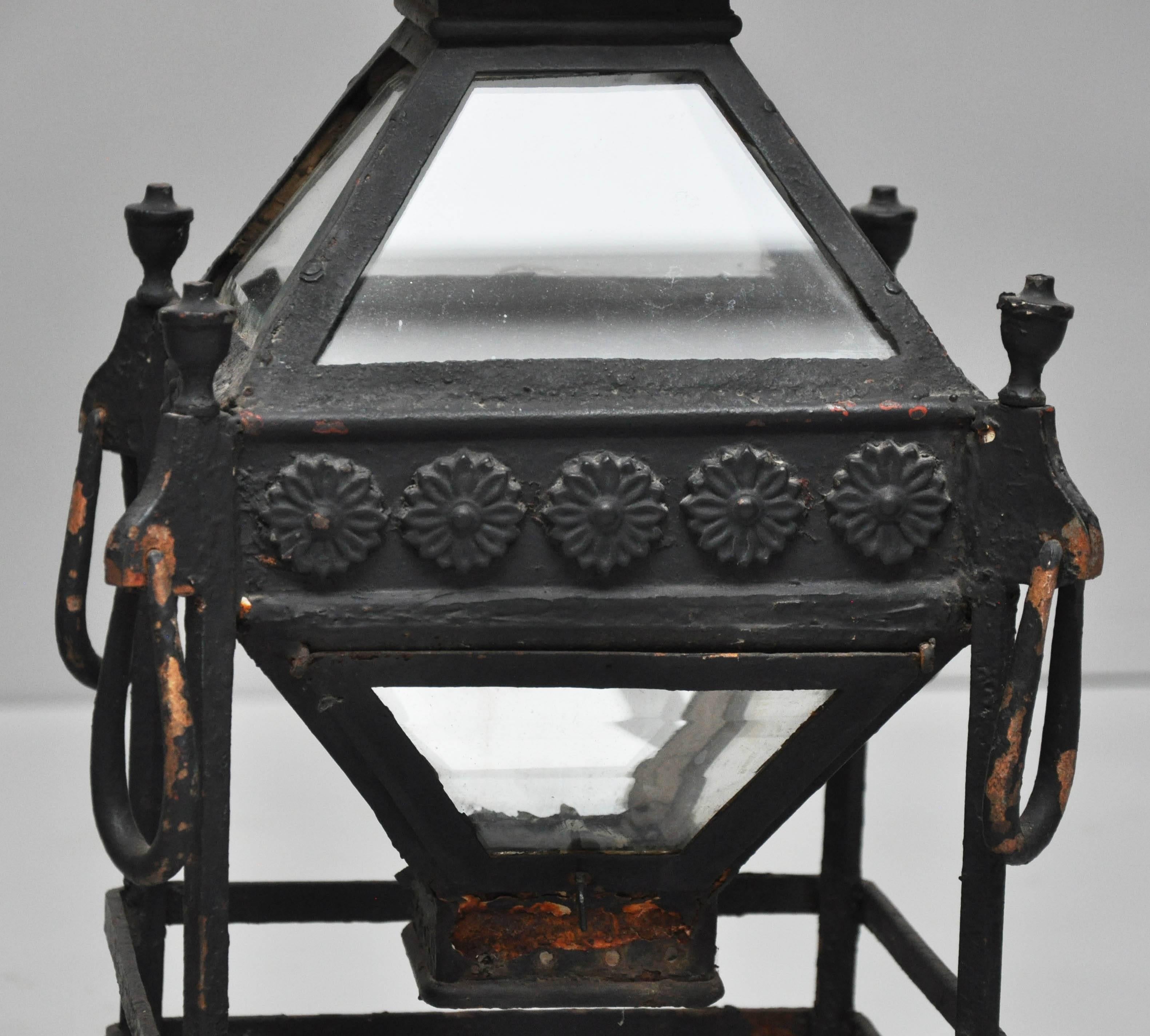 Pair of painted black iron and bronze pillar lanterns, square body in the shape of a pagoda, frieze with repeating flower head relief pattern, above polyhedral pyramid frame each side with beveled glass, surmounted by a four-sided flat pyramid cap,