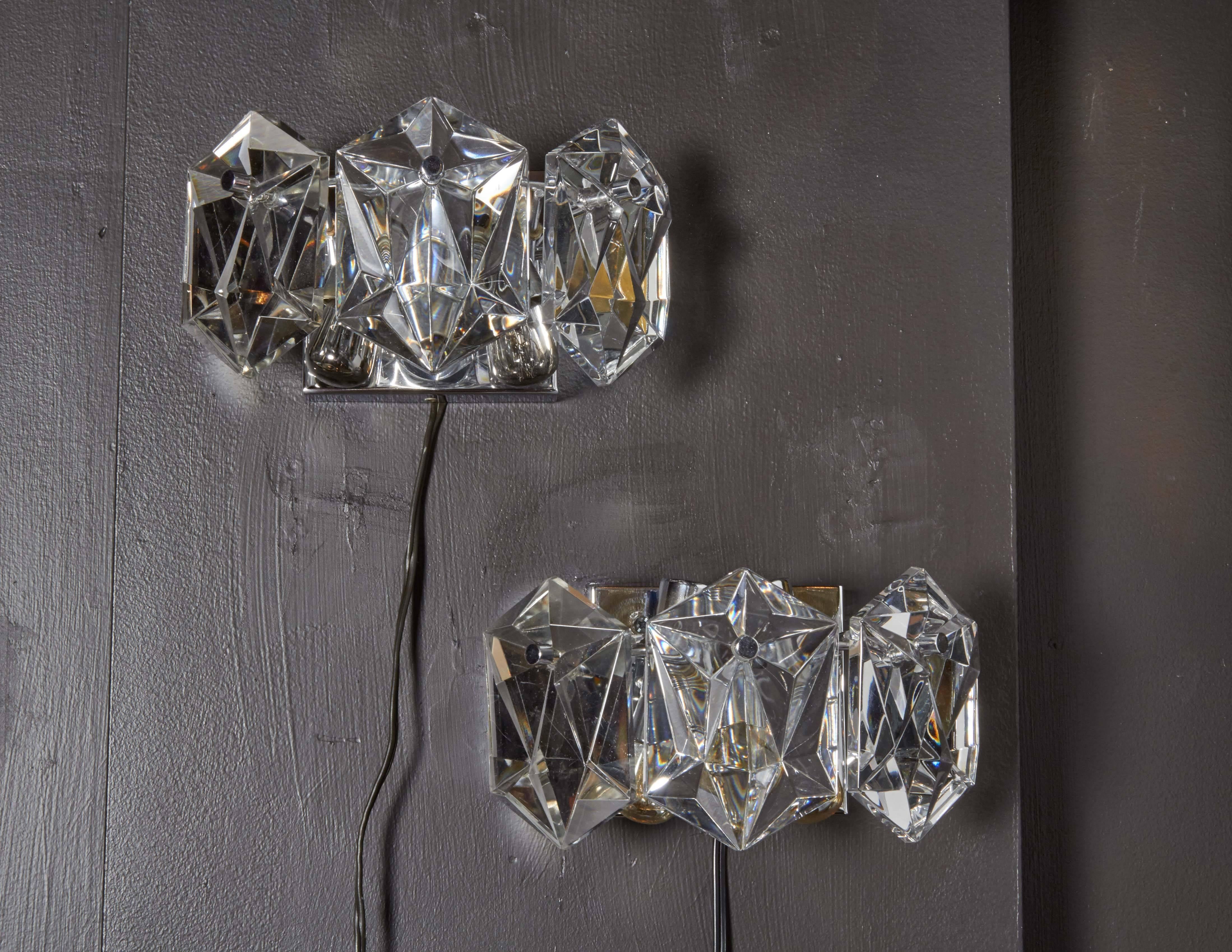 Pair of exquisite wall-mount lights, each featuring three faceted crystal prisms. Simple floating frames are finished in polished chrome with matching fittings, and have been newly rewired to accommodate two lights each. Perfect scale for powder