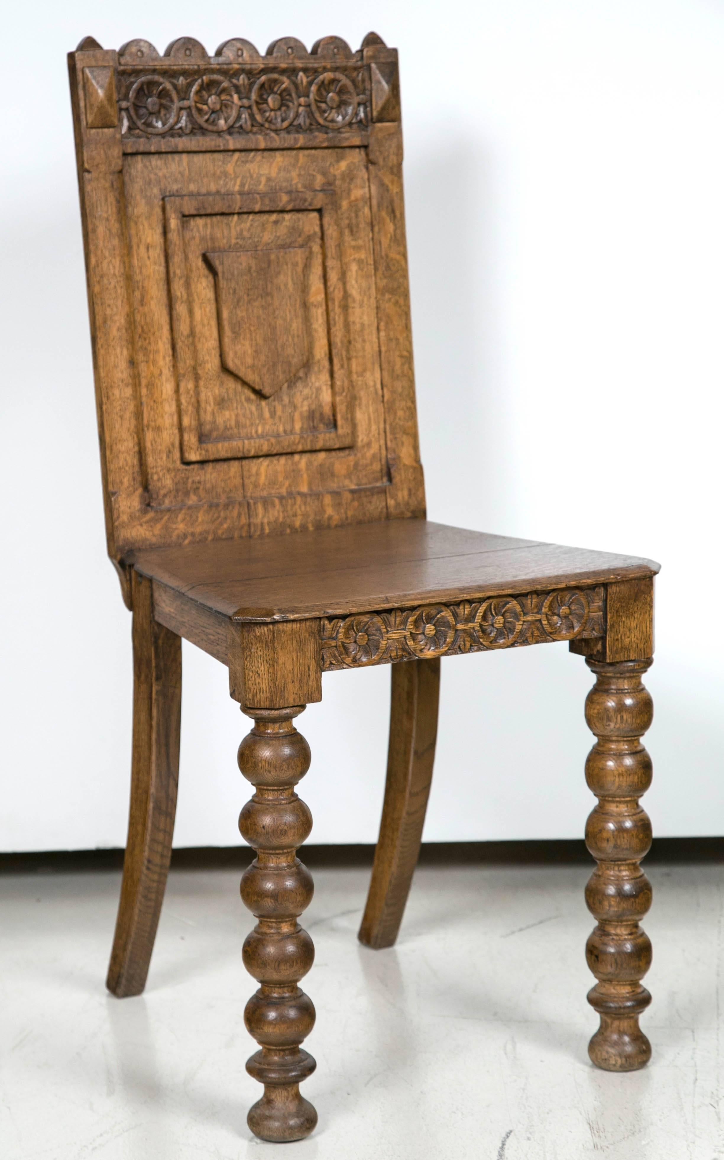 Antique, Germanic hall chair has decorative carvings on back and on the apron. Carvings include a shield and additional details. One split in the wood seat but in good condition.
